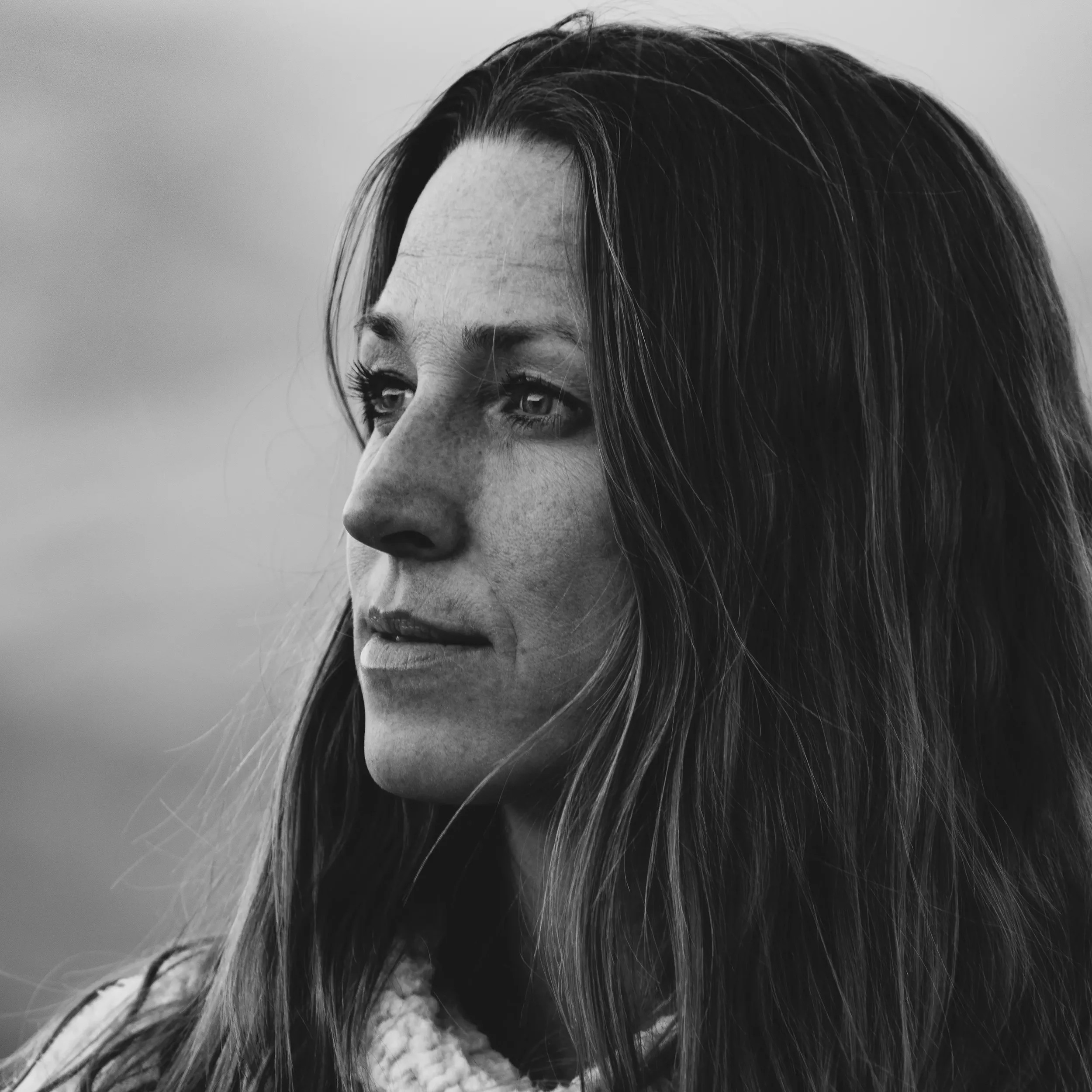 Close-up black and white photo of a woman's face, showing her eyes, nose, and part of her forehead and cheek, with long hair partially covering her face.