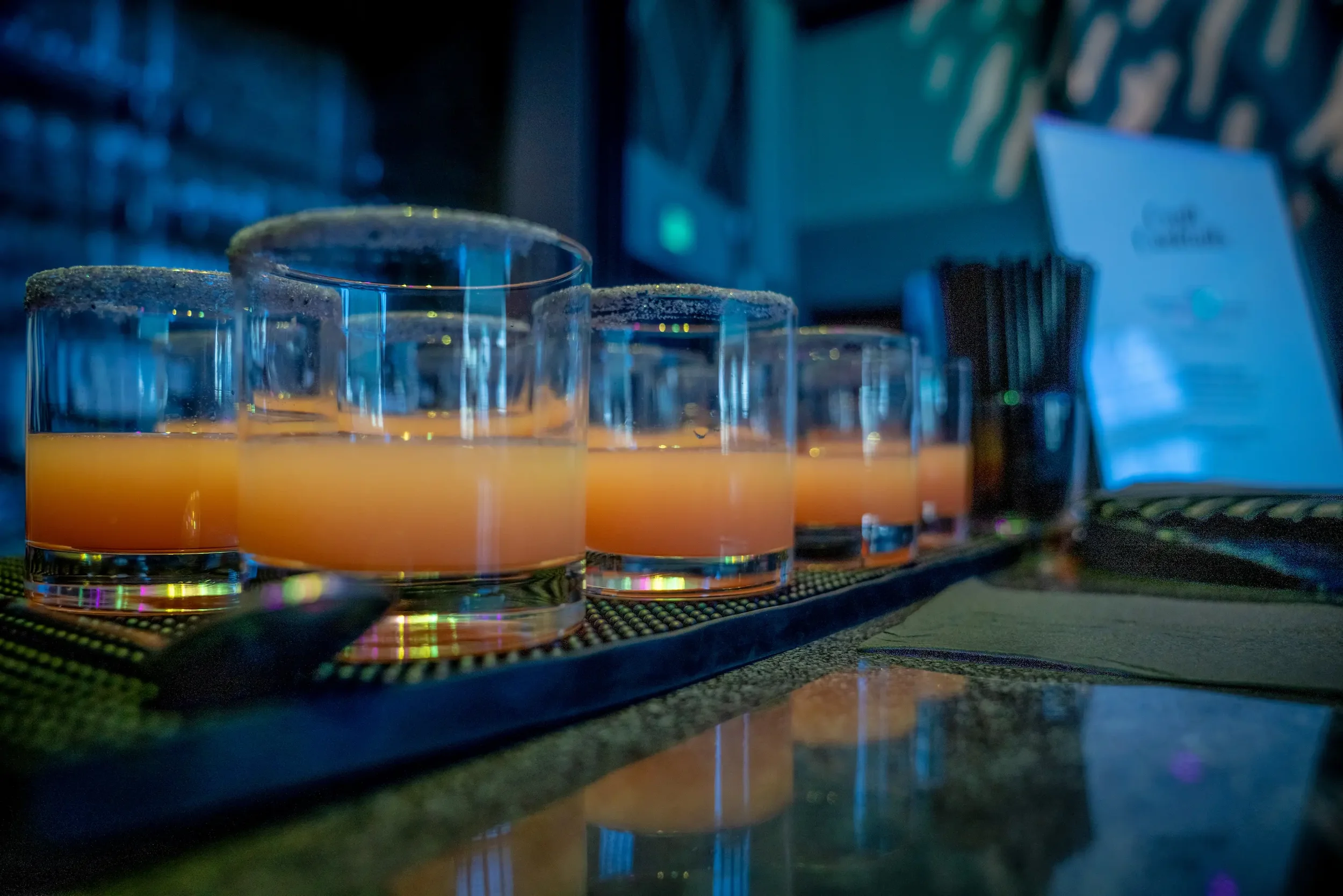 Several shot glasses filled with an orange-colored liquid, likely in a bar or restaurant setting.