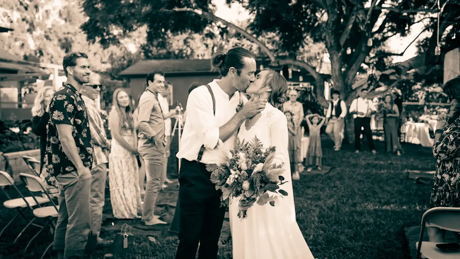 Bride and groom sharing their first kiss as guests look on at a backyard ceremony