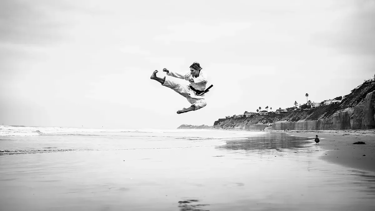 Martial artist mid-air throwing a flying kick on an empty beach