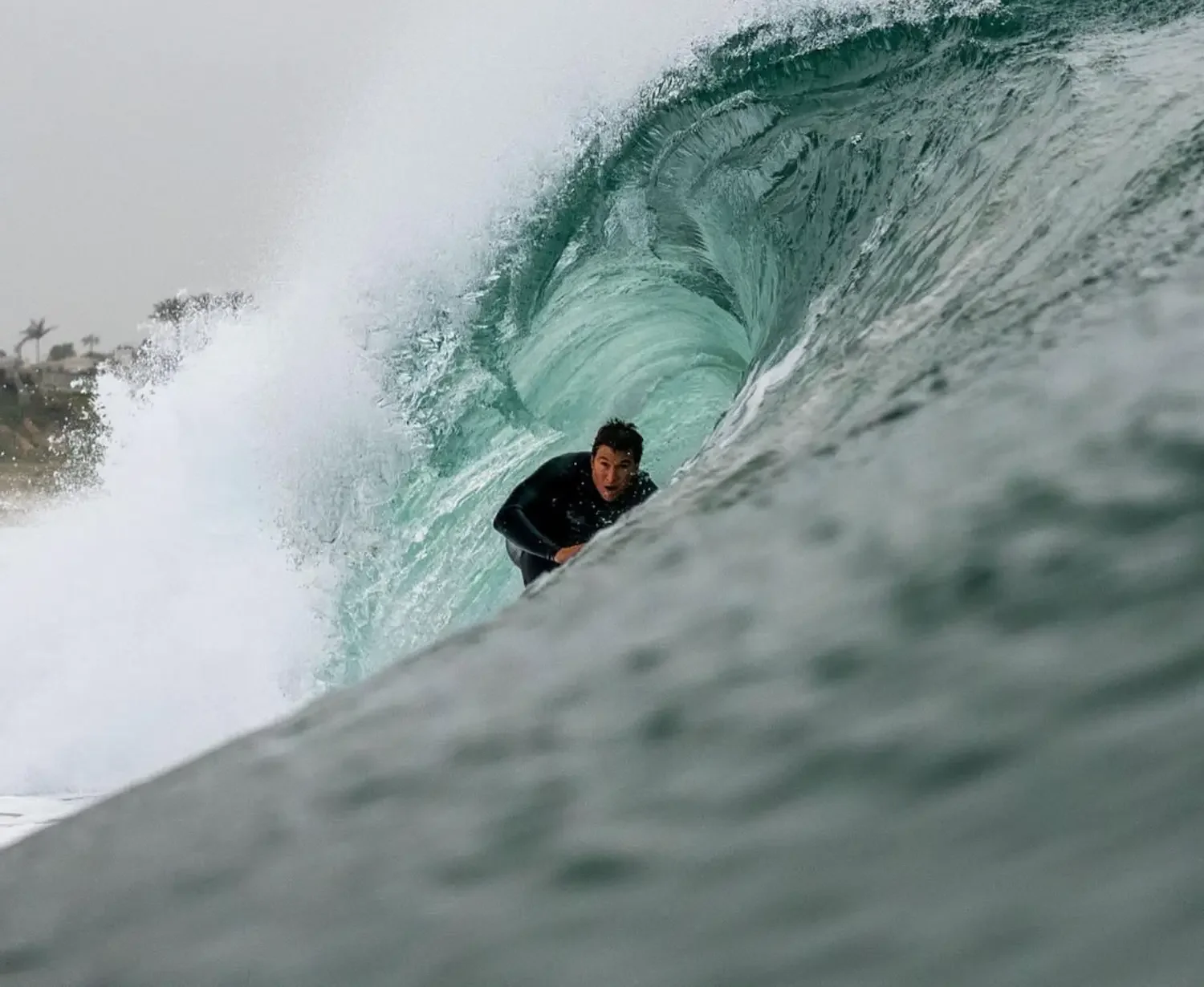 Surfer crouched low, riding inside the hollow curl of a breaking wave