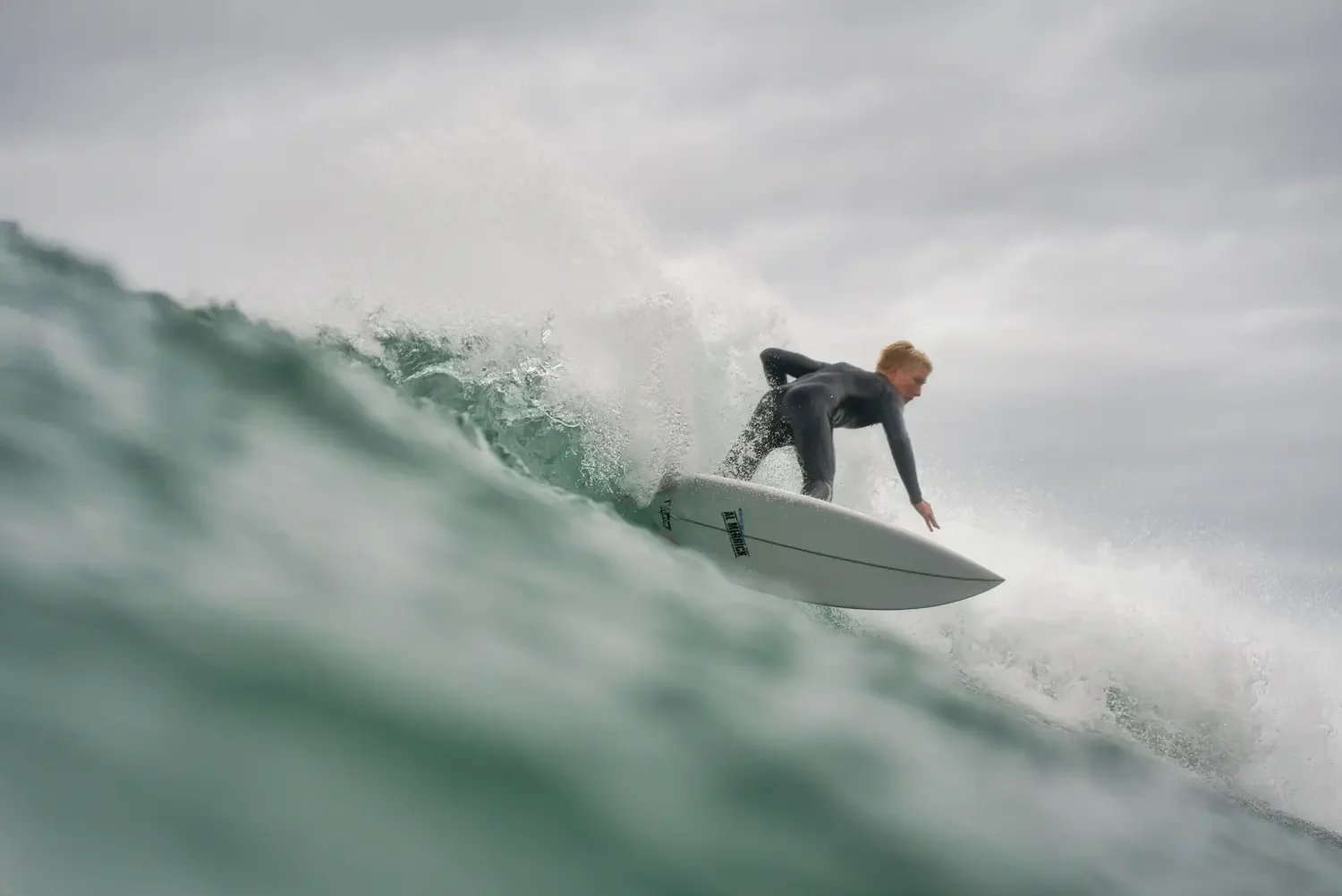 A woman surfing on a wave in the ocean during overcast weather.