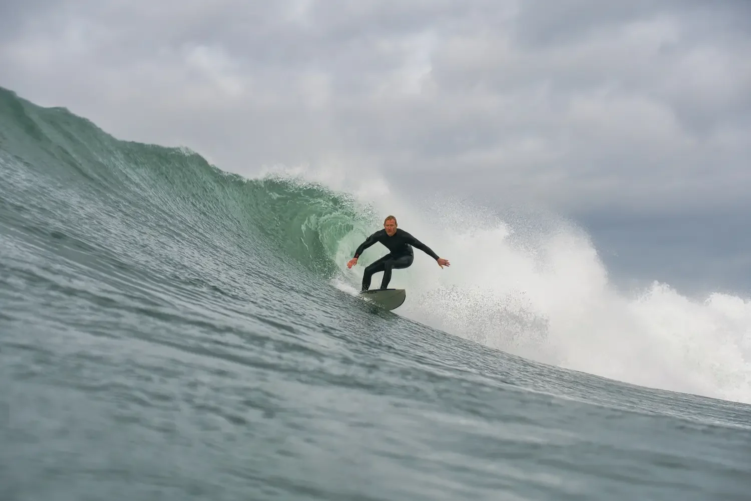 A man surfing on a large ocean wave during cloudy weather