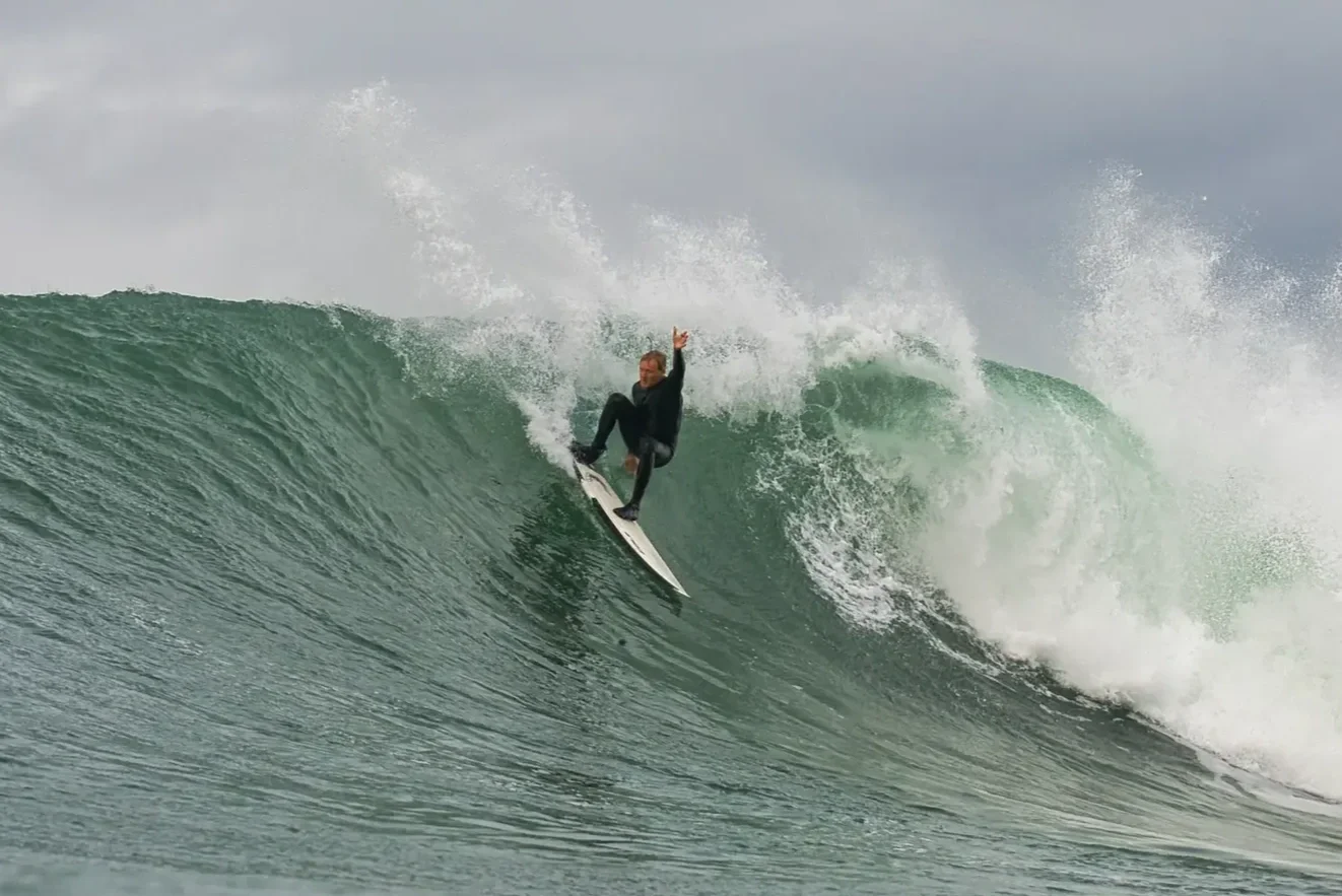 A person surfing on a large wave in the ocean under a cloudy sky.