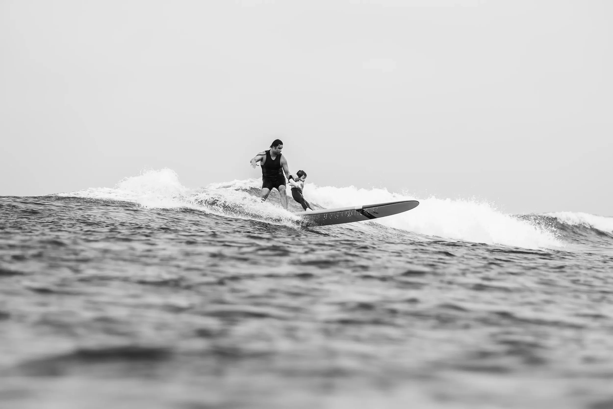 A man and a young girl surfing on a wave in the ocean, black and white photography.