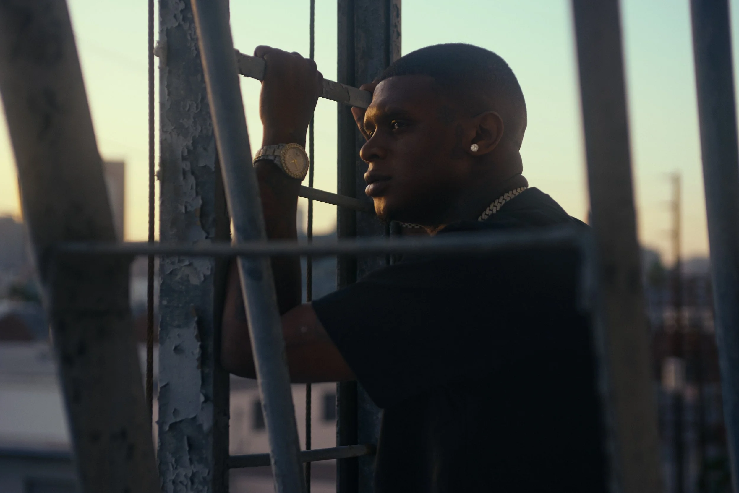 A man holding onto a metal railing on a rooftop during sunset, demonstrating a contemplative mood.