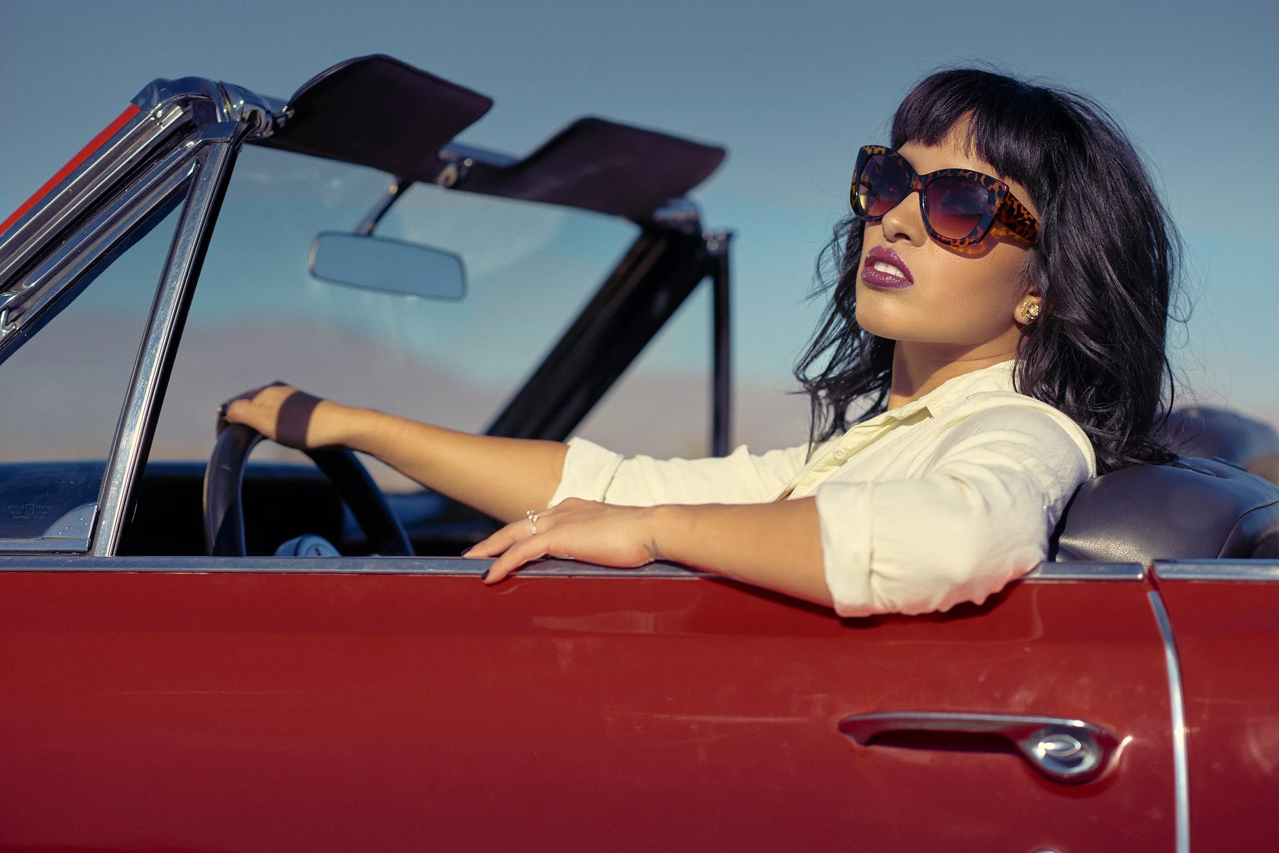 Lisa Jennigs wearing oversized sunglasses inside a red vintage convertible during the WESTBOUND fashion story.