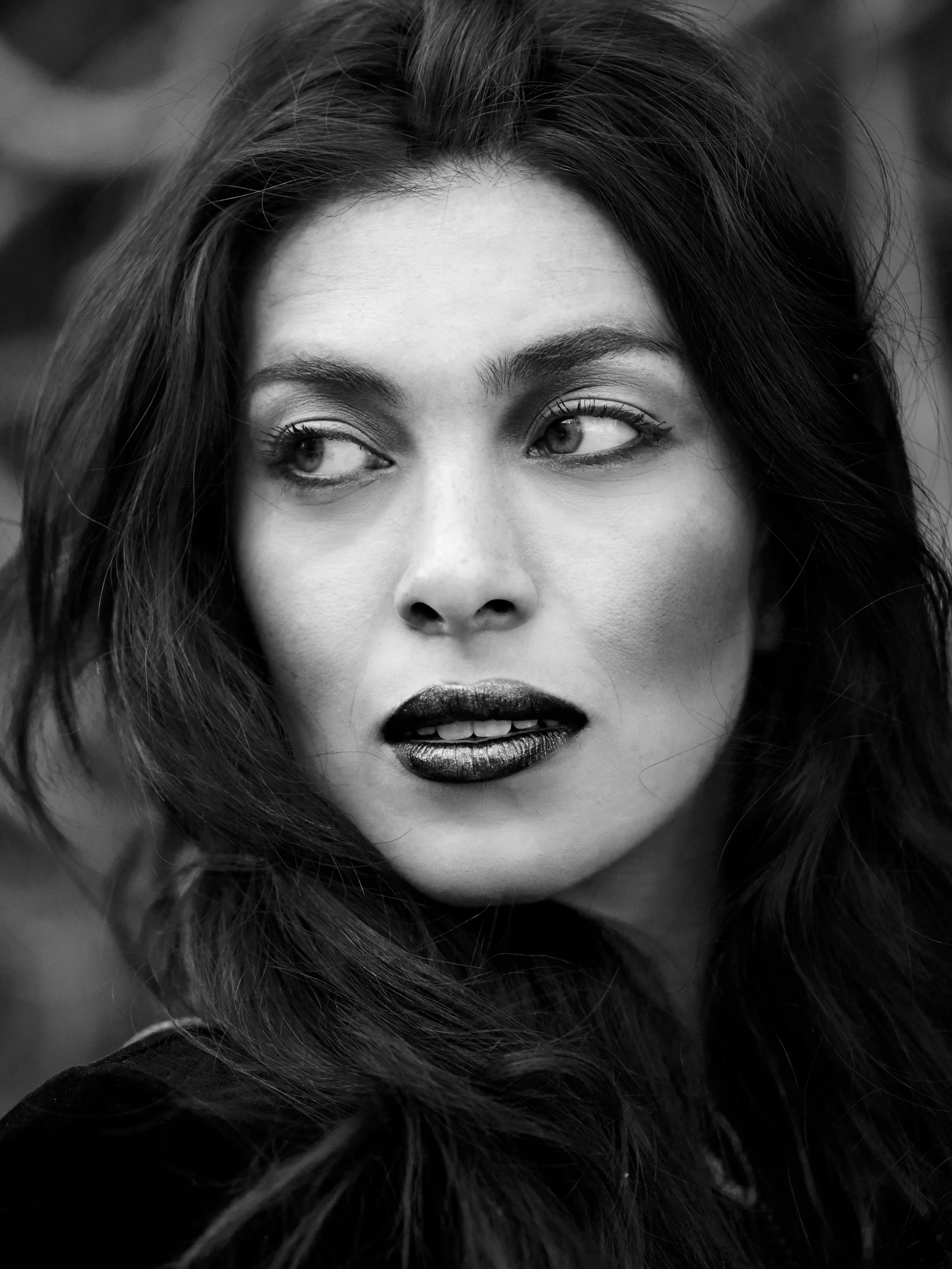 Close-up black-and-white portrait of a woman with wavy hair, partially covering her face, looking to the side.