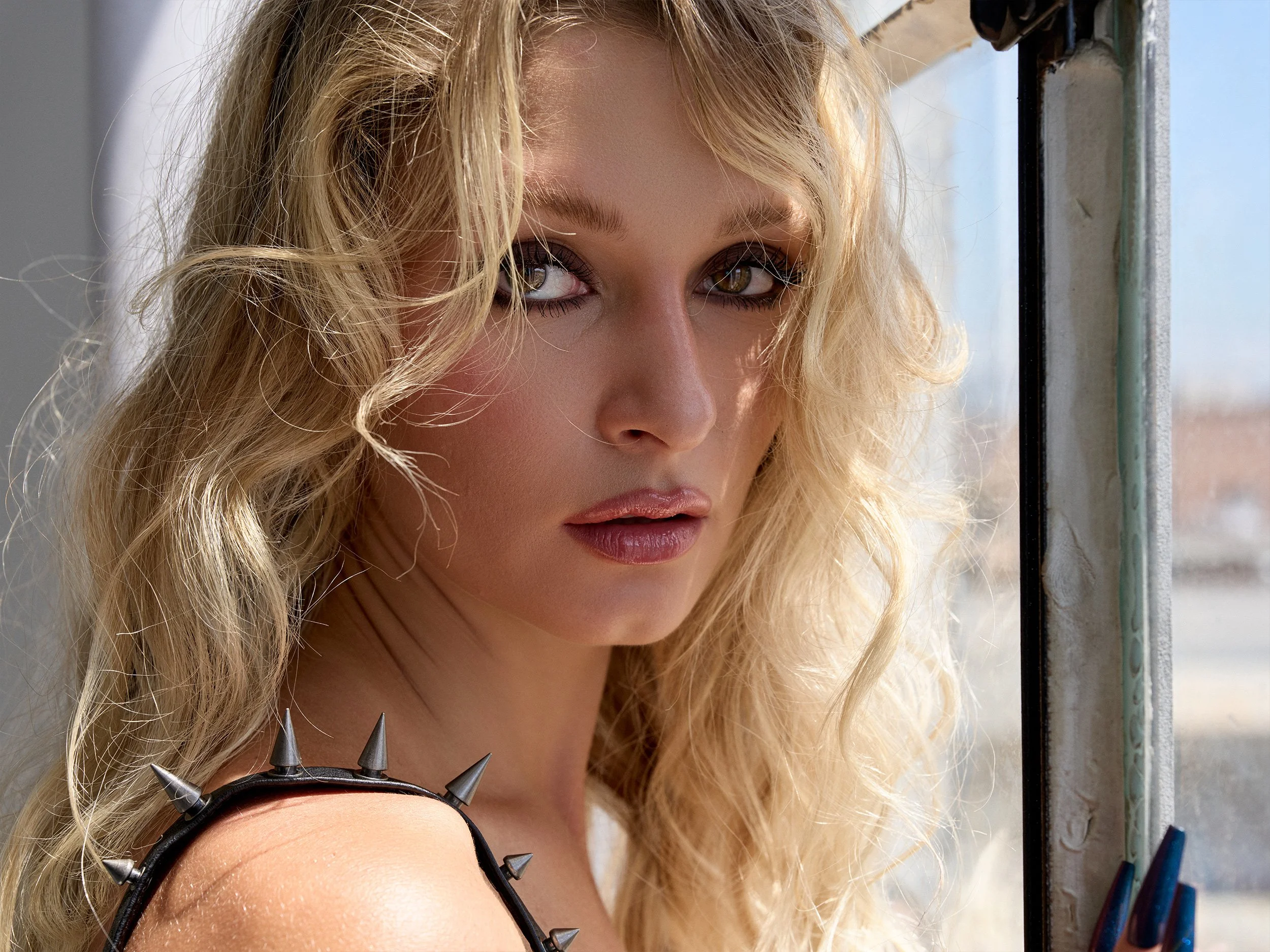 Close-up beauty portrait of model Katherine Kiss with spiked black leather styling and loose blonde hair by Los Angeles photographer Aram Kay.