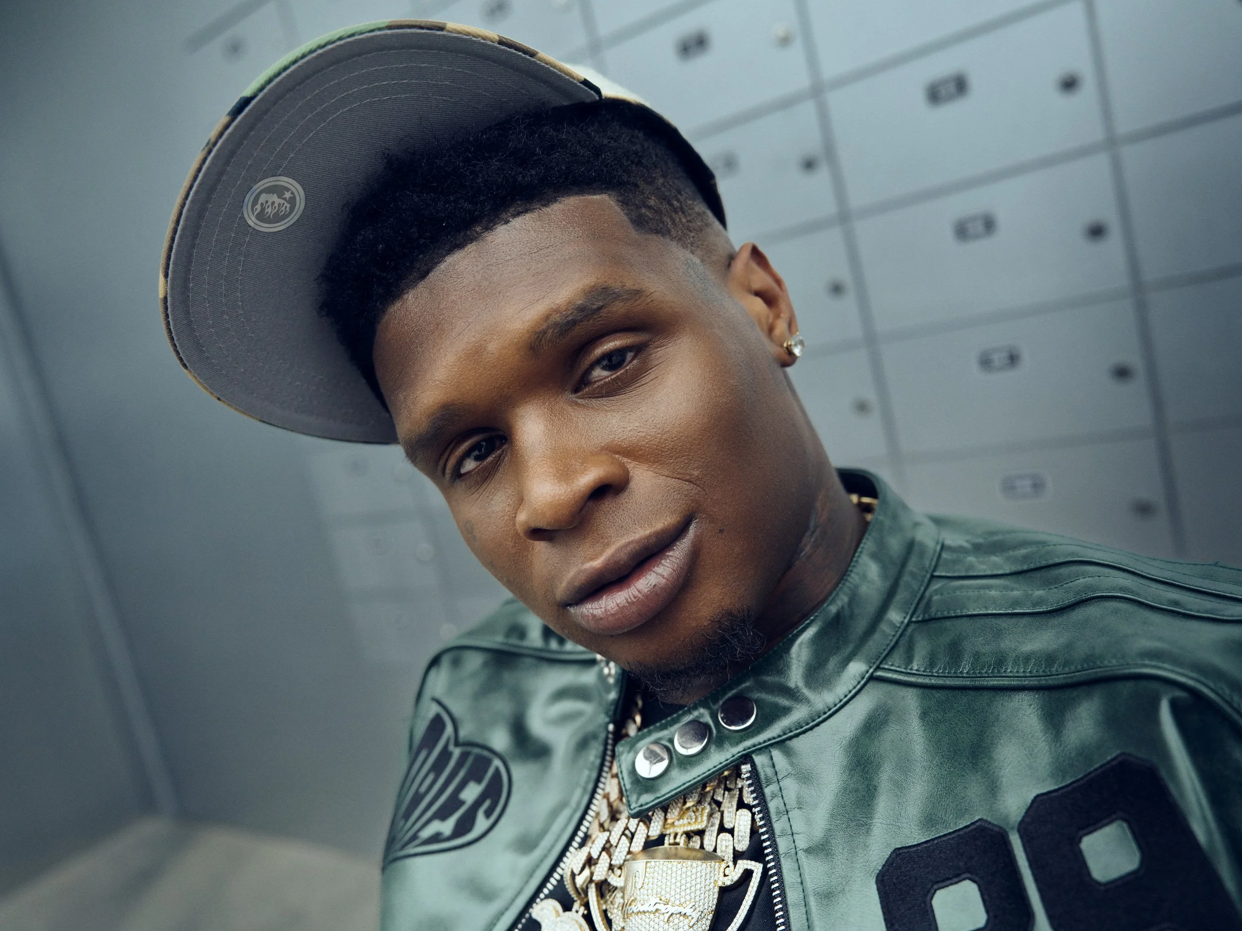 Close portrait of recording artist HoodTrophy Bino wearing a dark green leather jacket and cap