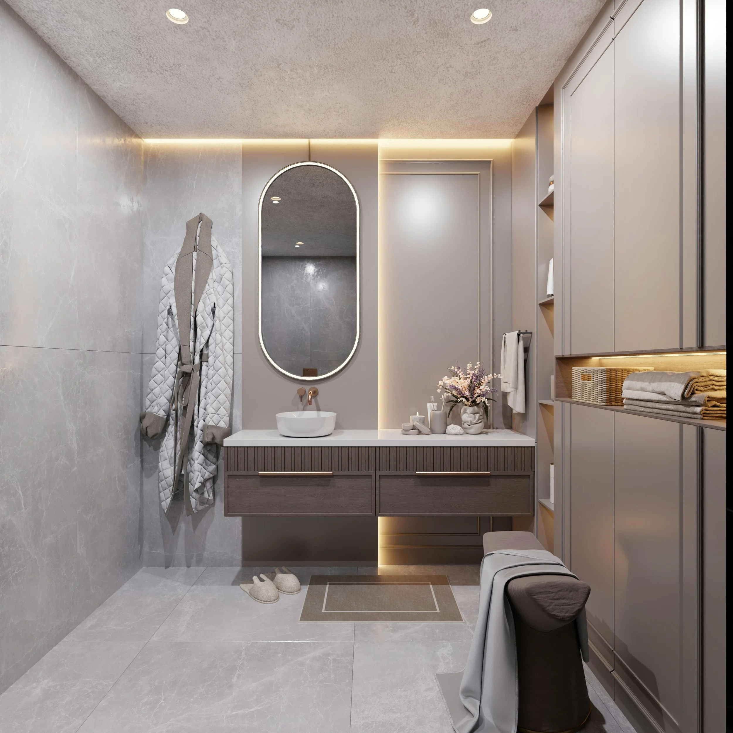 A modern, minimalist bathroom with light gray tiled flooring and walls, a floating vanity with a round vessel sink, a large oval mirror with backlit LED lighting, a small stool with a cushion, a folded towel on an open shelf, and a coat hanging on a hook. There are ceiling recessed lights and a potted plant with pink flowers on the vanity.