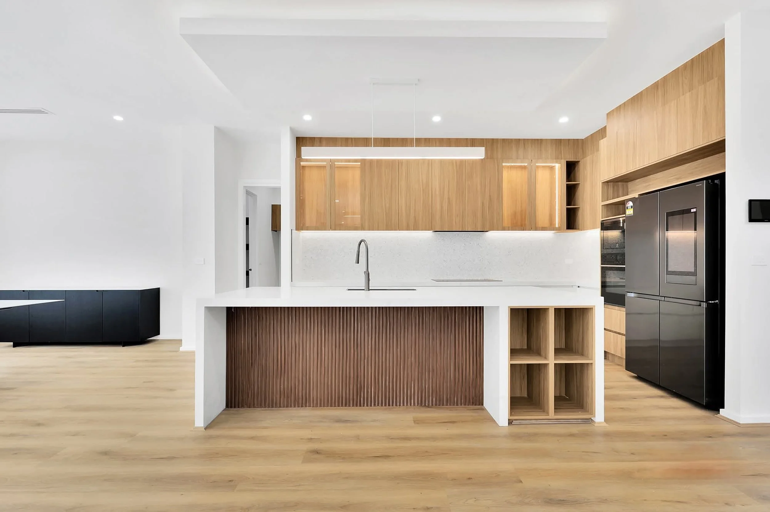 Modern kitchen with white countertops, wooden cabinets, black appliances, and light hardwood flooring.