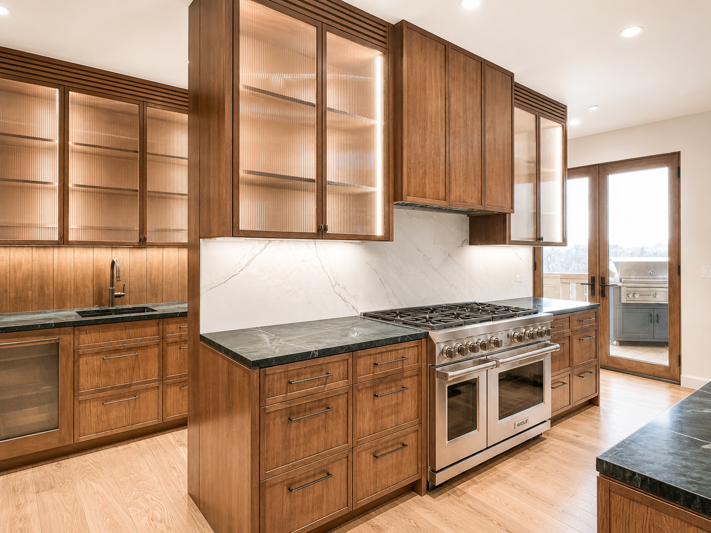Modern kitchen with wooden cabinets, black countertops, stainless steel appliances, and a marble backsplash. Features a stove, oven, and a door leading to an outdoor grilling area.