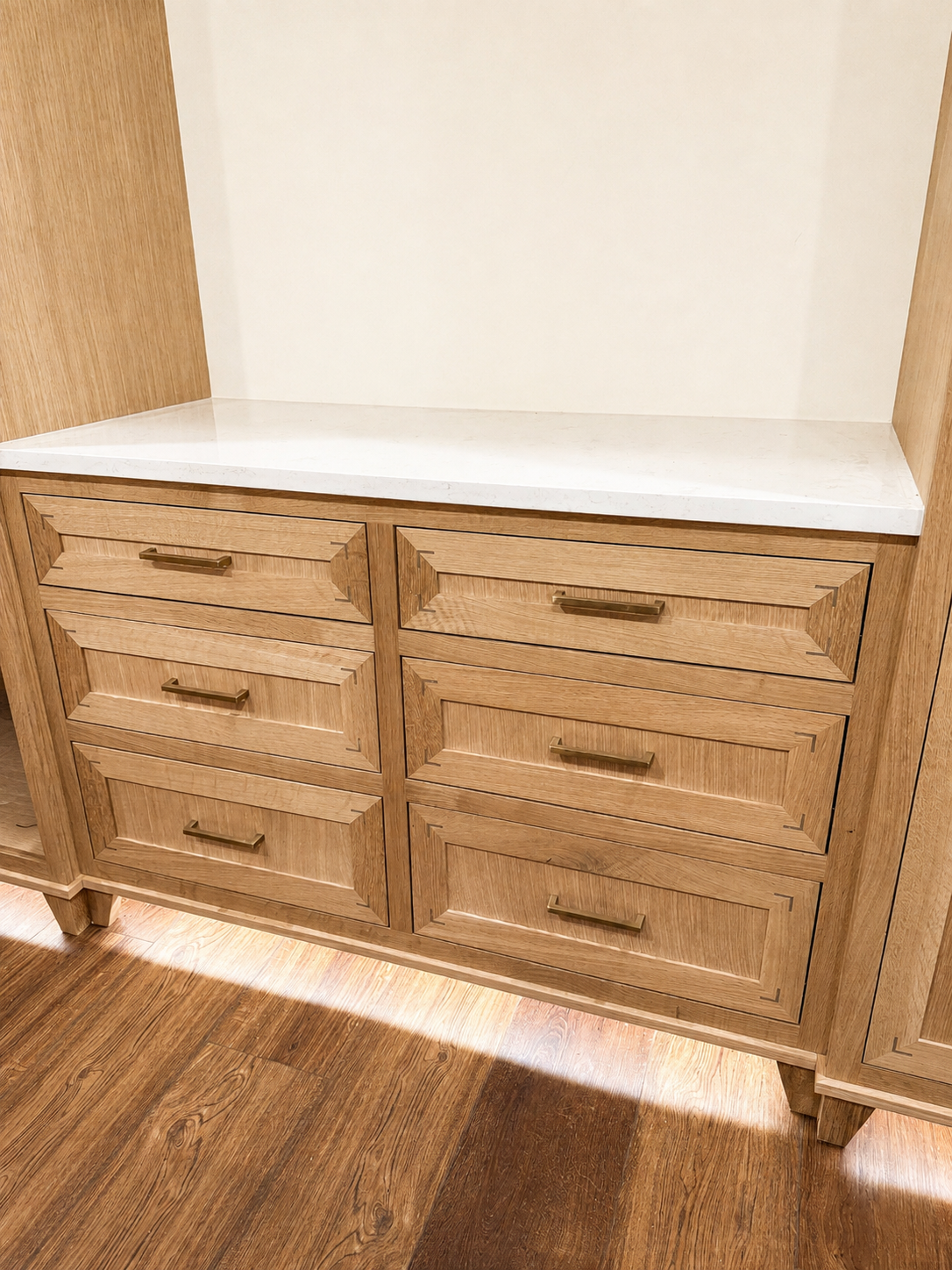 Wooden cabinet with six drawers and gold handles, topped with white marble countertop, against a white wall and wooden floor.
