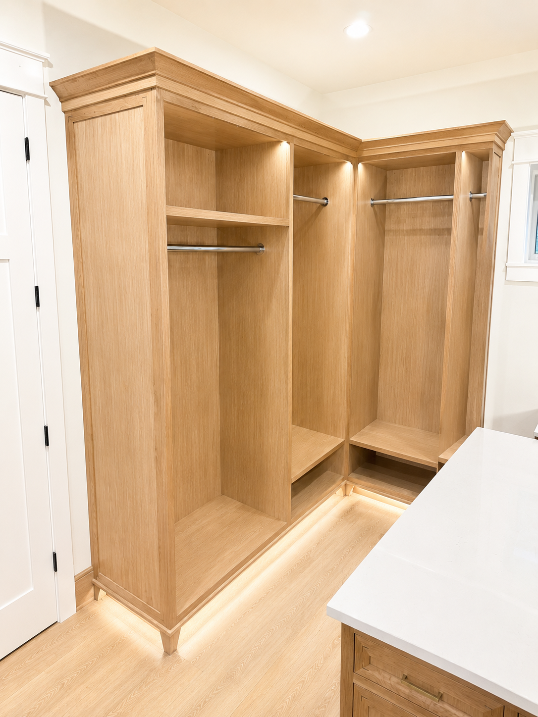 Empty wooden walk-in closet with two hanging rods, a shelf, and LED lighting at the base.