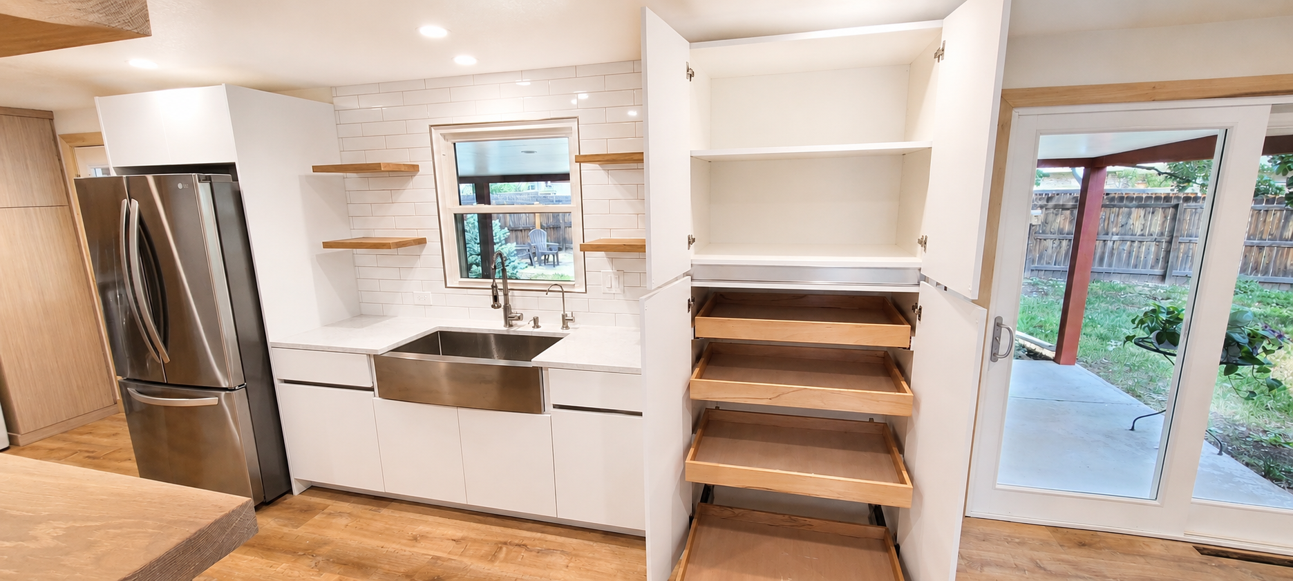 Kitchen with white cabinets, a stainless steel refrigerator, open shelves, a window over a farmhouse sink, and a sliding glass door leading to a backyard.