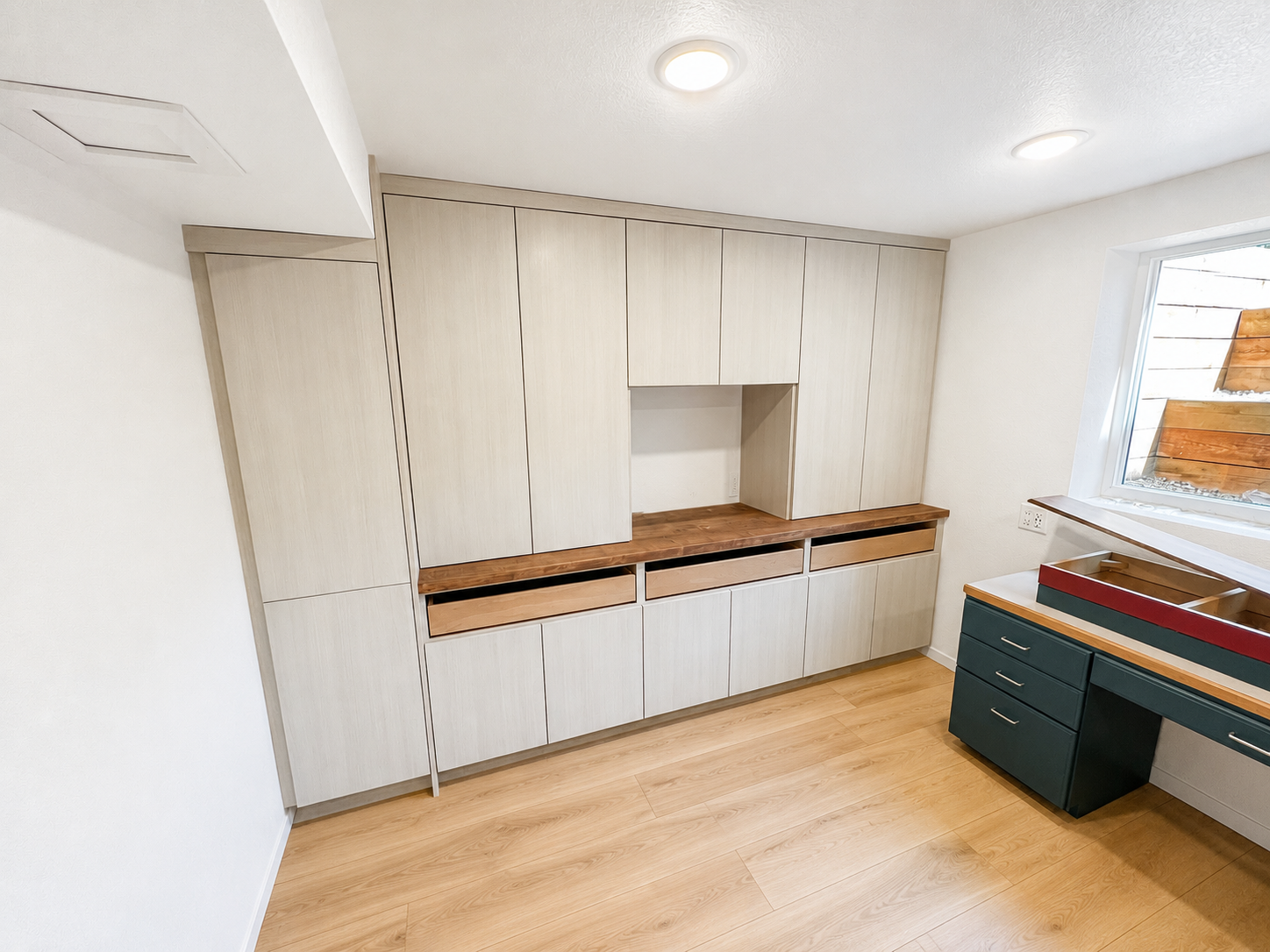 Interior of a room with light wood cabinetry, a wooden work surface, and a window with wooden shutters.