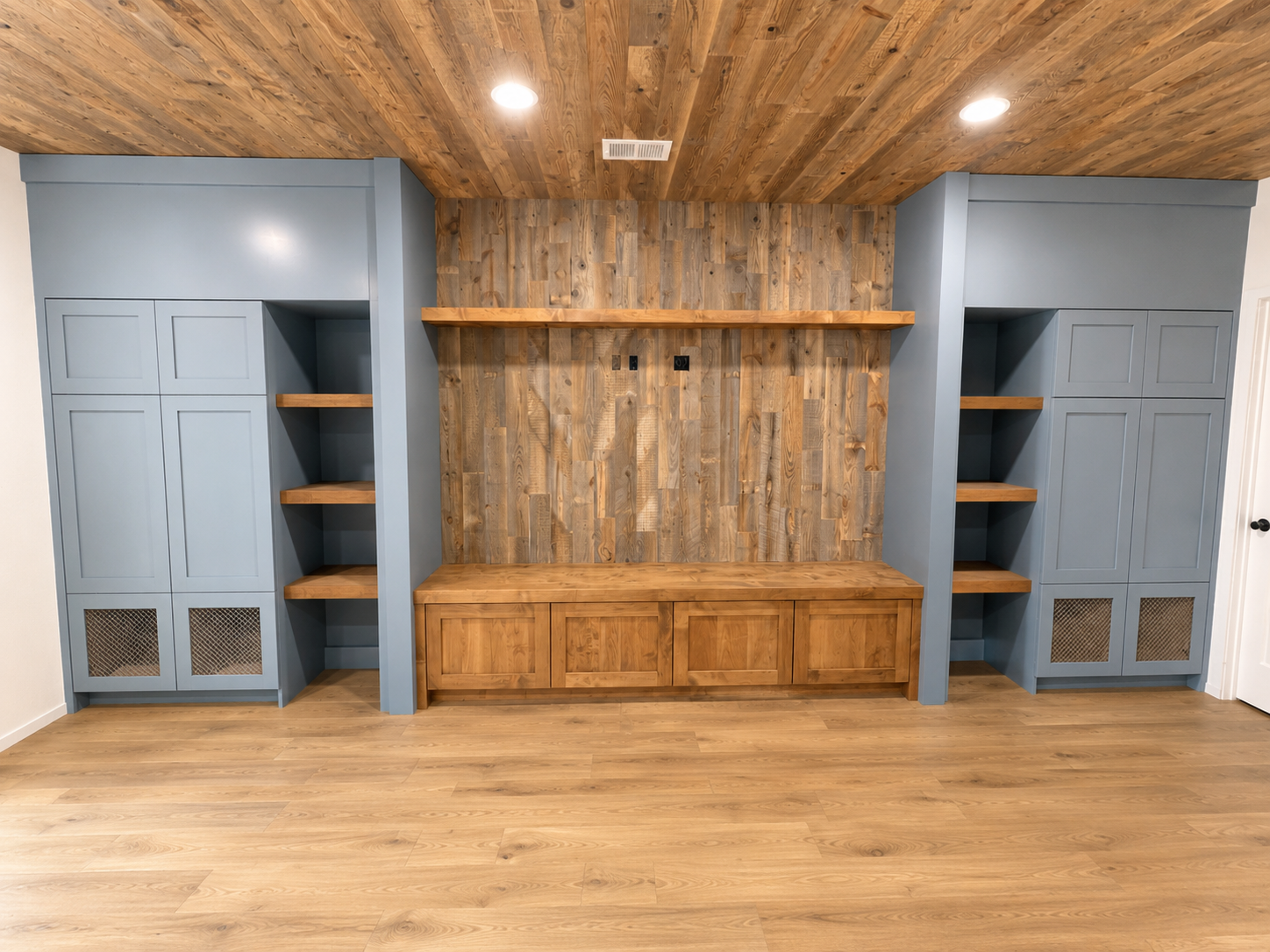 Living room wall with built-in blue cabinets, open shelves, a wooden bench, and a wood-paneled wall and ceiling, with recessed lighting.