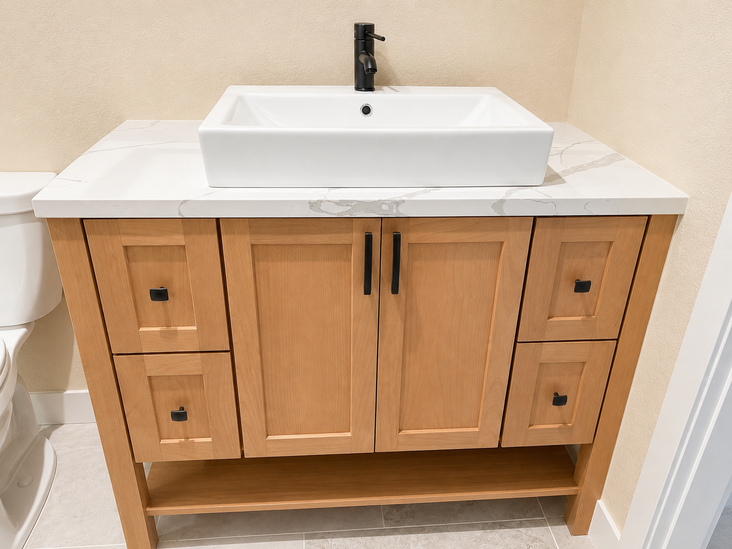 Bathroom vanity with a white rectangular sink, black faucet, wooden cabinet with black handles, and beige wall.