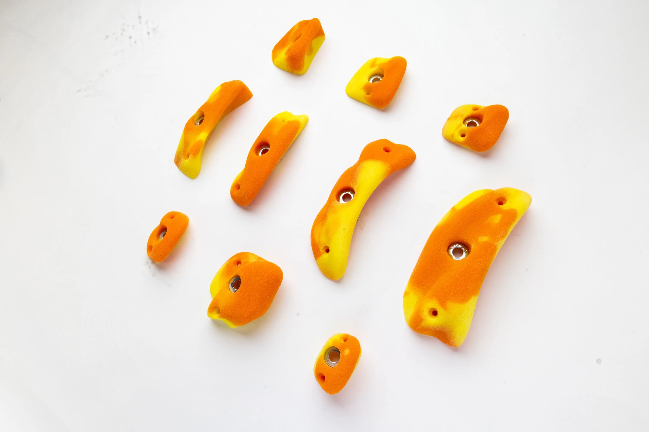 Climbing holds of various shapes and sizes in yellow and orange colors scattered on a white surface.
