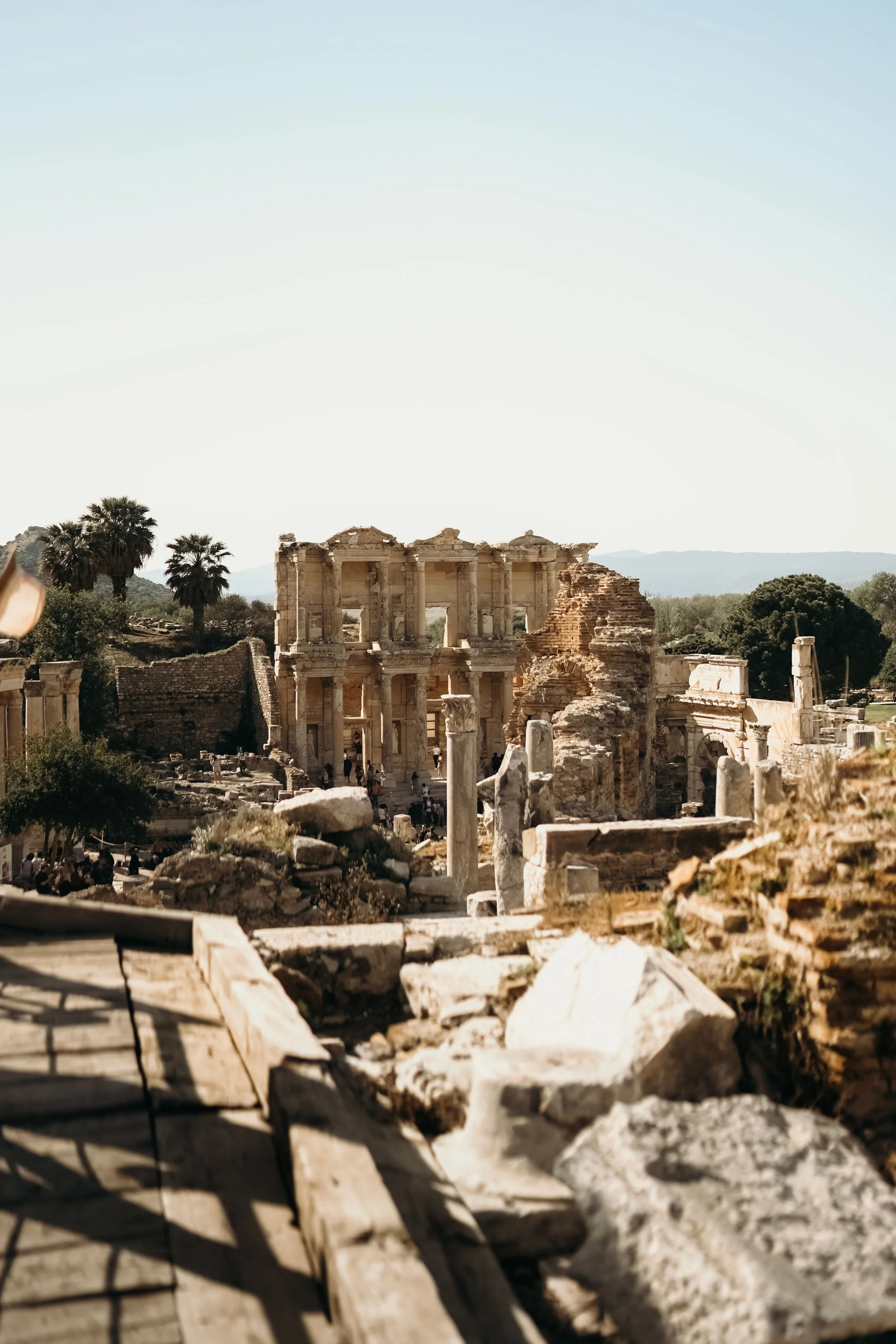 Ancient ruins of a Roman theater with columns and stone structures, surrounded by trees and mountains in the background under a clear sky.