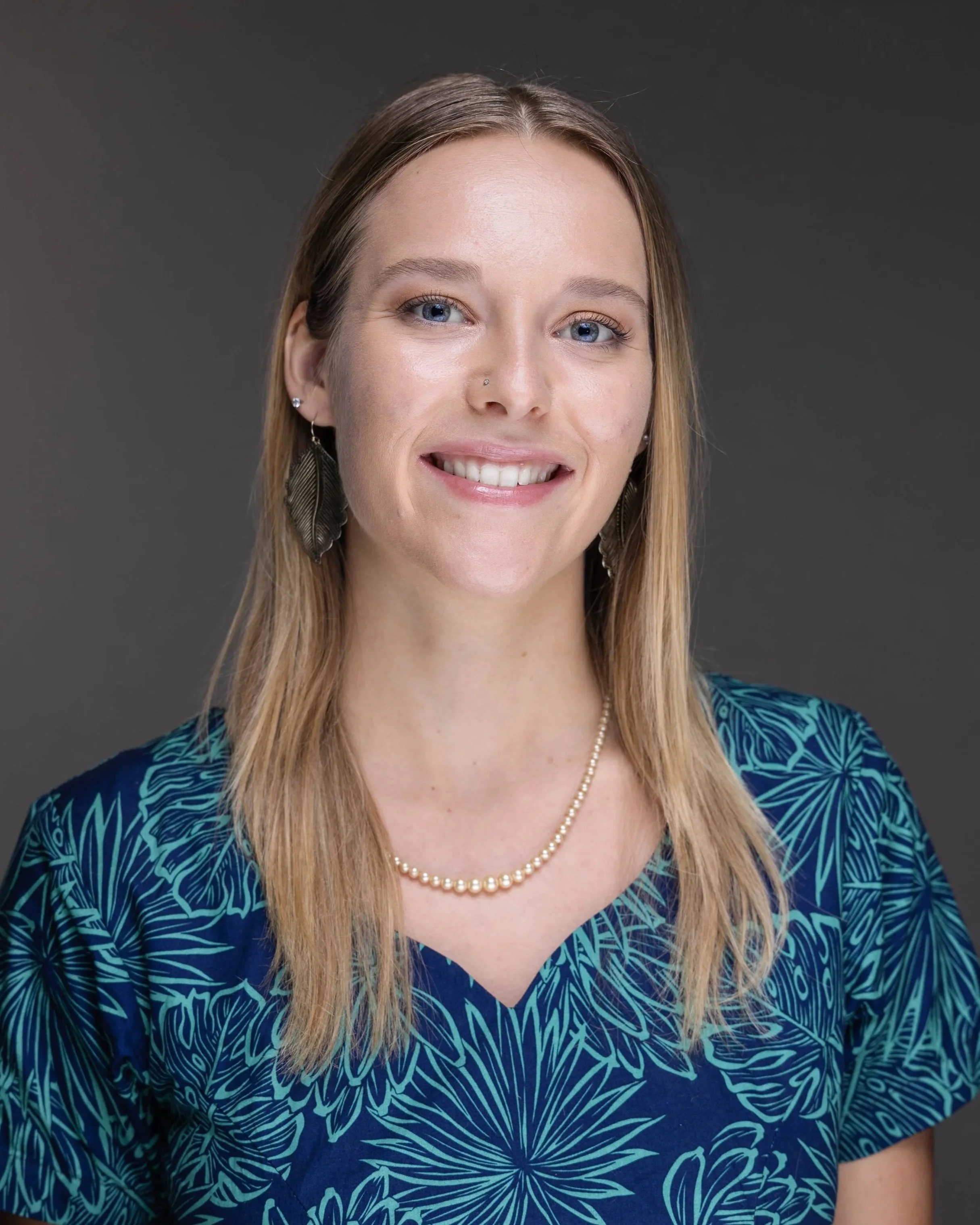 Headshot of a founder and CEO, Alyssa Garvin. She has long blonde hair, blue eyes, earrings, a pearl necklace, and a blue patterned top, smiling against a dark background.