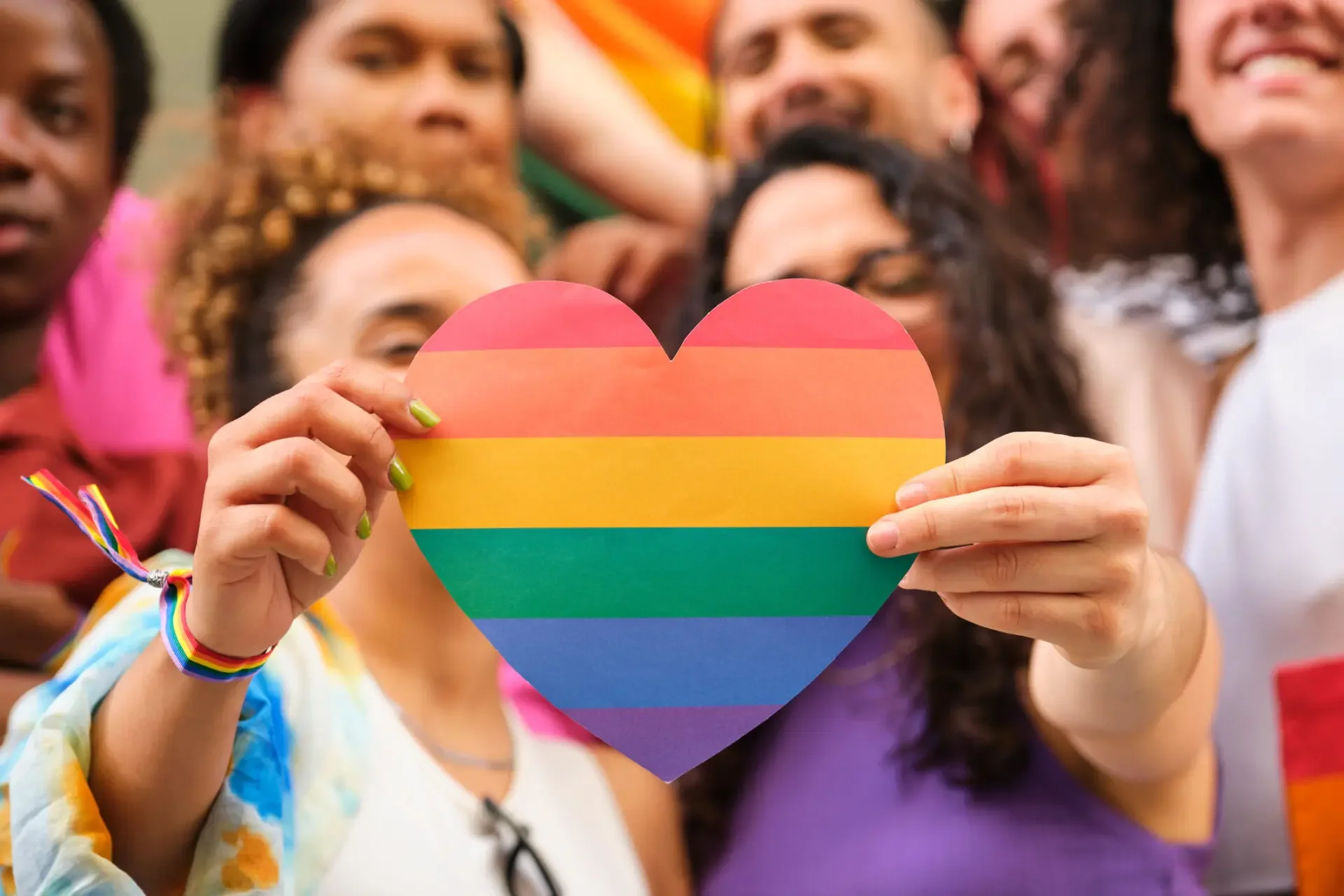 Group of diverse people holding a rainbow-colored heart symbol at a pride event.