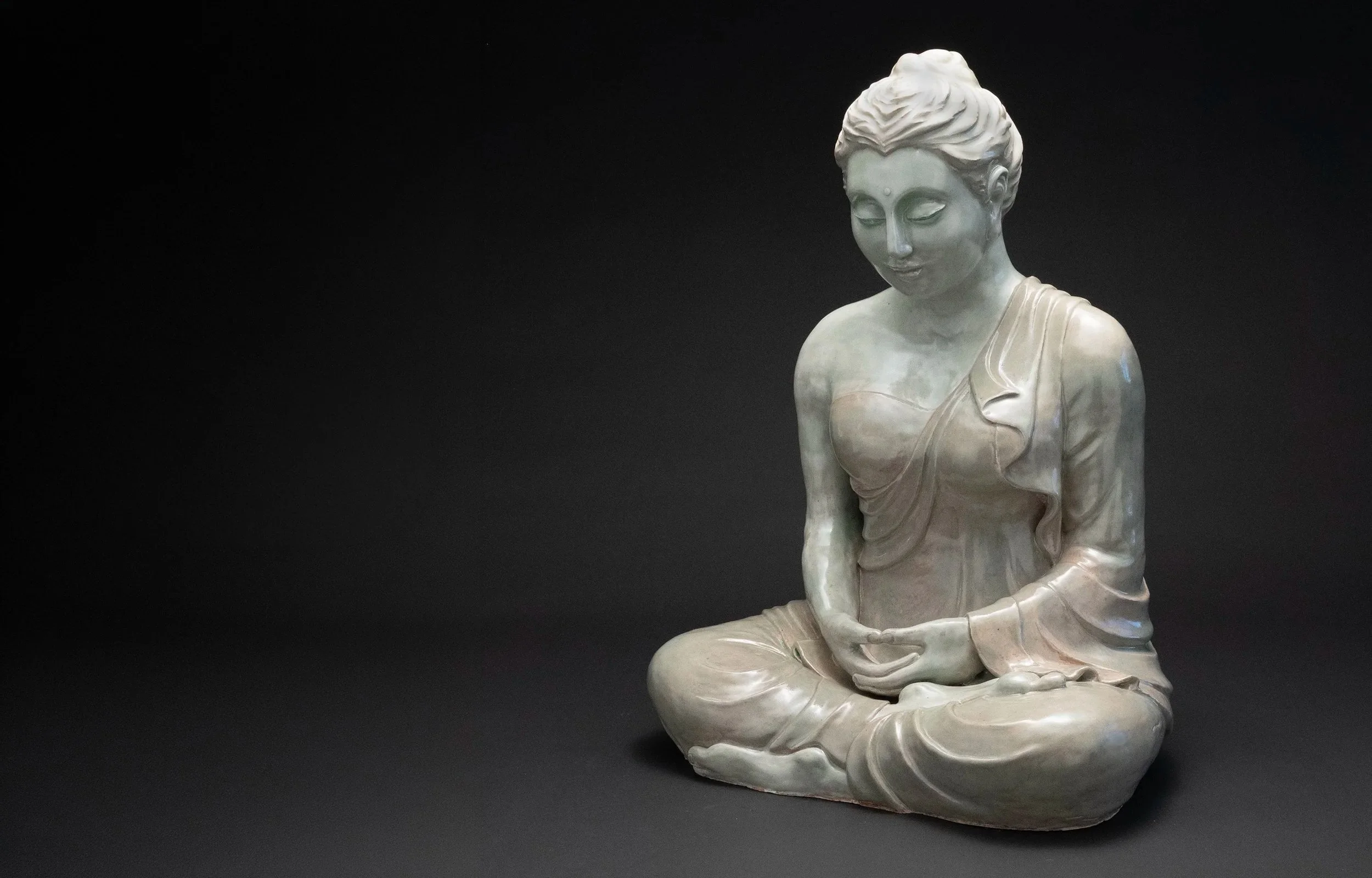 Marble sculpture of a seated woman with serene expression, leaf-patterned dress, and braided hair, against a dark background.