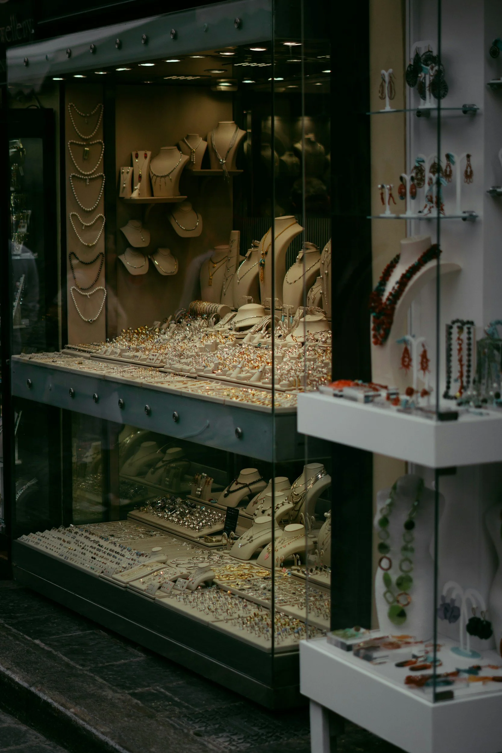 Jewelry store display window featuring various necklaces, bracelets, earrings, and rings on mannequin busts and jewelry stands.