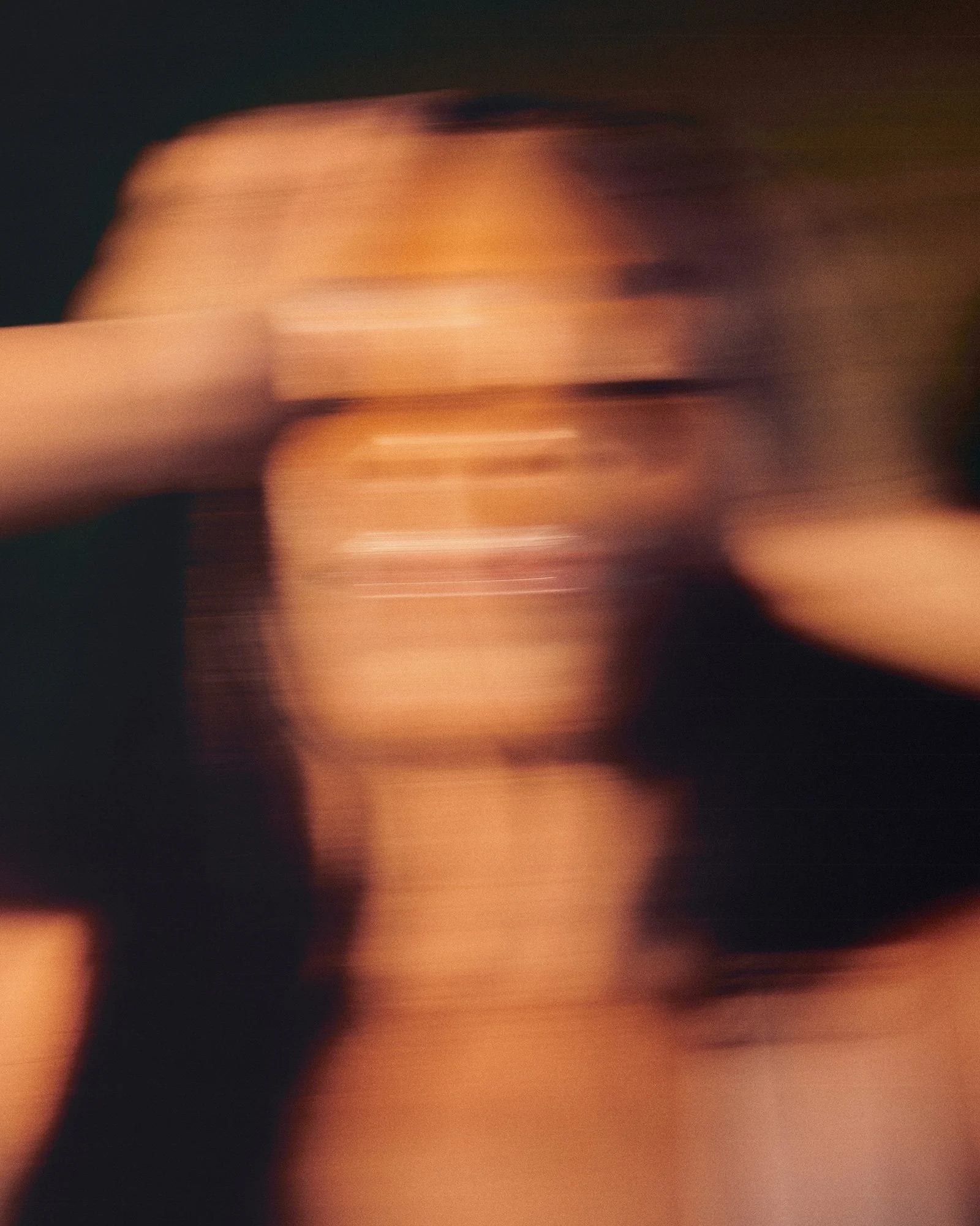 A person with dark, voluminous hair covering their face, wearing a black top, with a blurred background.
