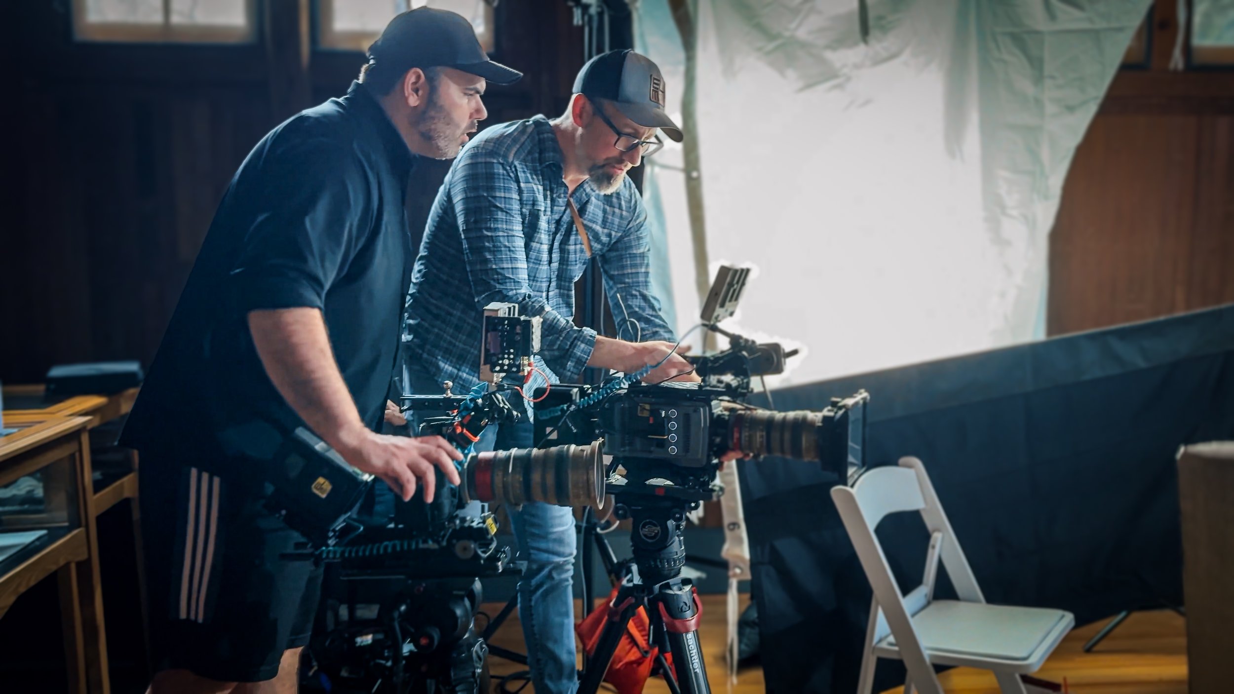 Darren Durlach and DP Jonathan Mount operating a professional film camera on a set, one adjusting the equipment and the other observing, with lighting and set decorations in the background.