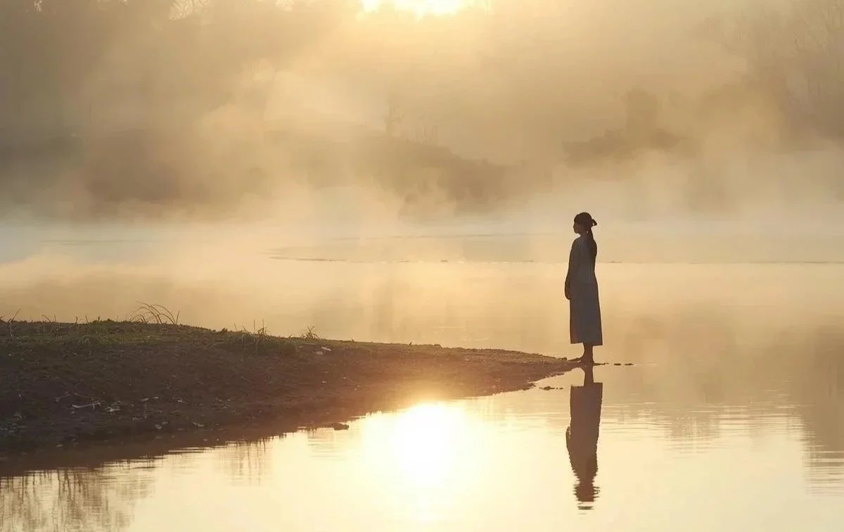 A person standing by a calm lake during a quiet moment of self-reflection.