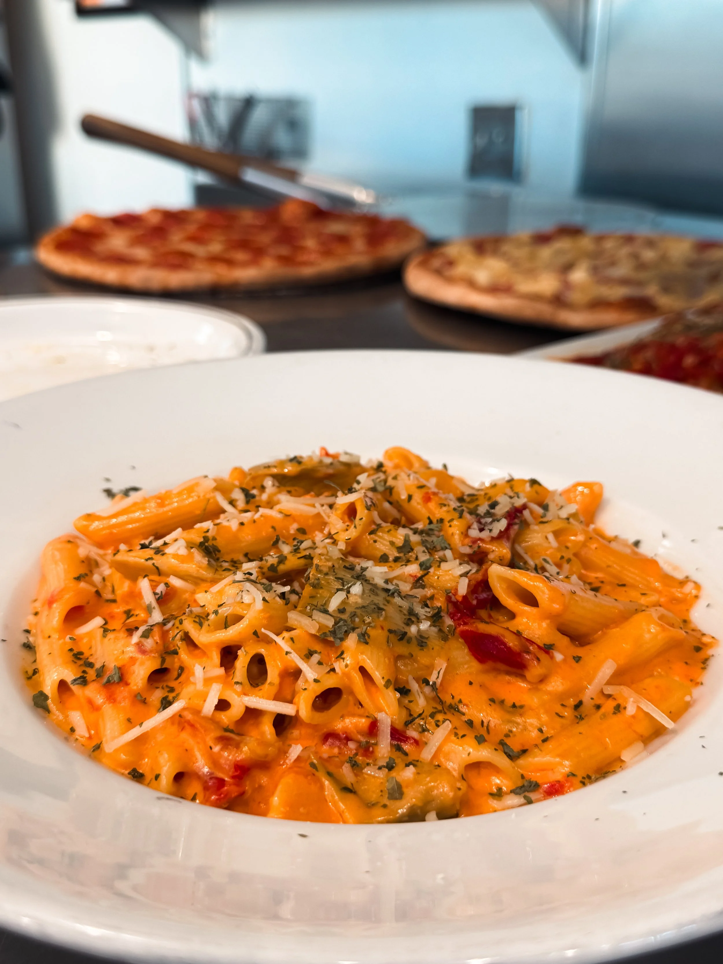 Plated pasta with tomato sauce, grated cheese, and herbs, inside a white bowl