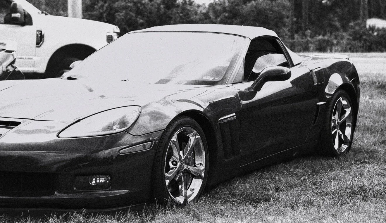 Black sports car with sleek design, parked on grass near other vehicles, black and white photo.