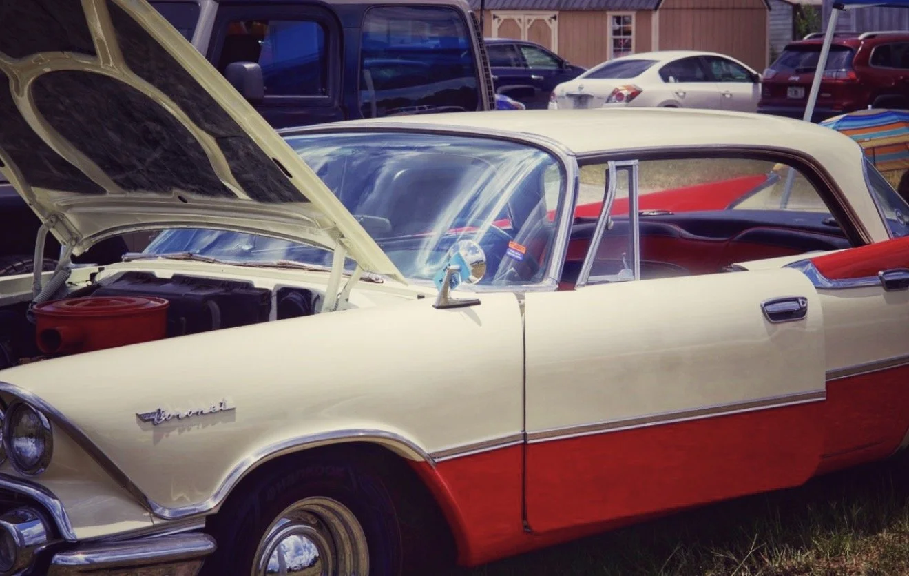 A vintage cream and red two-tone Chevrolet car with its hood open, parked at a car show or outdoor gathering.