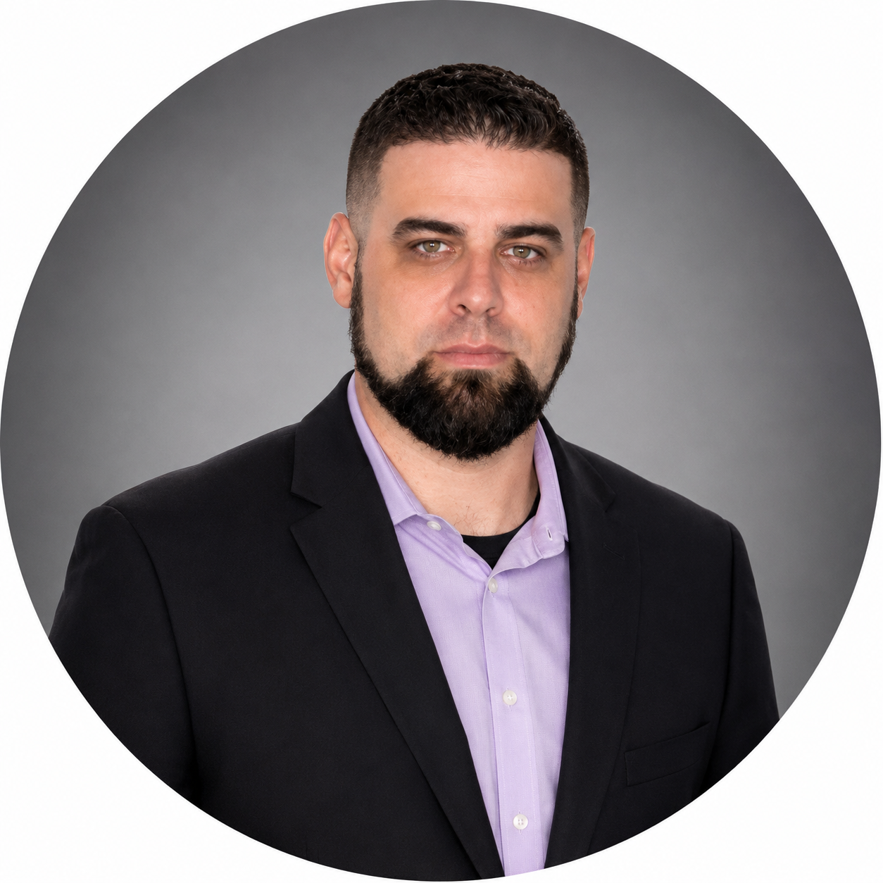 Headshot of a man with short dark hair, a beard and mustache, wearing a black blazer and a light purple dress shirt, against a gray background.