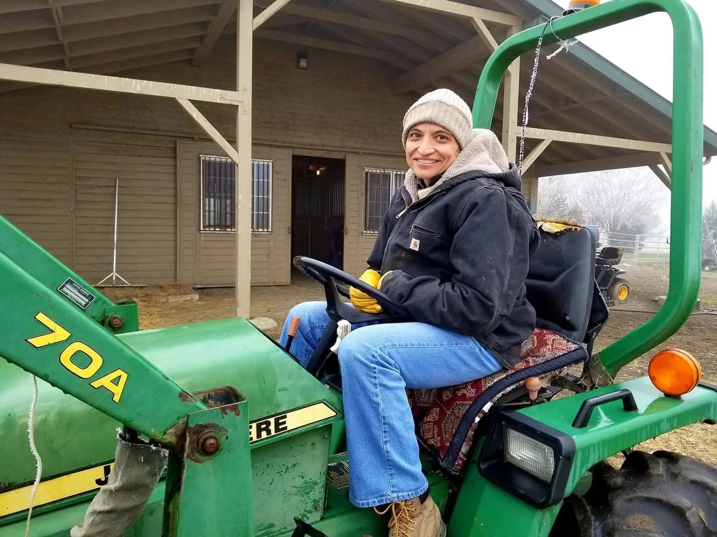 Janelle Carman-Wagner (JCW) sitting on a tractor tending to her horses in the winter.