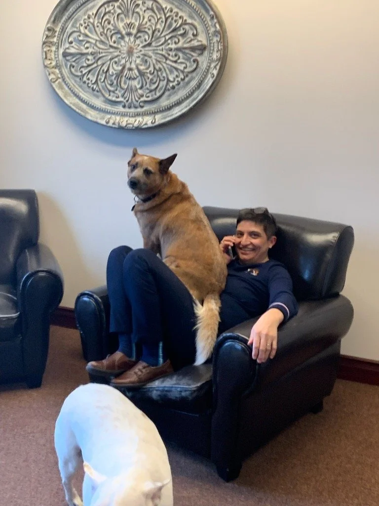 Janelle Carman-Wagner (JCW) sitting on a comfy chair with her dog in her lap while she takes a phone call.
