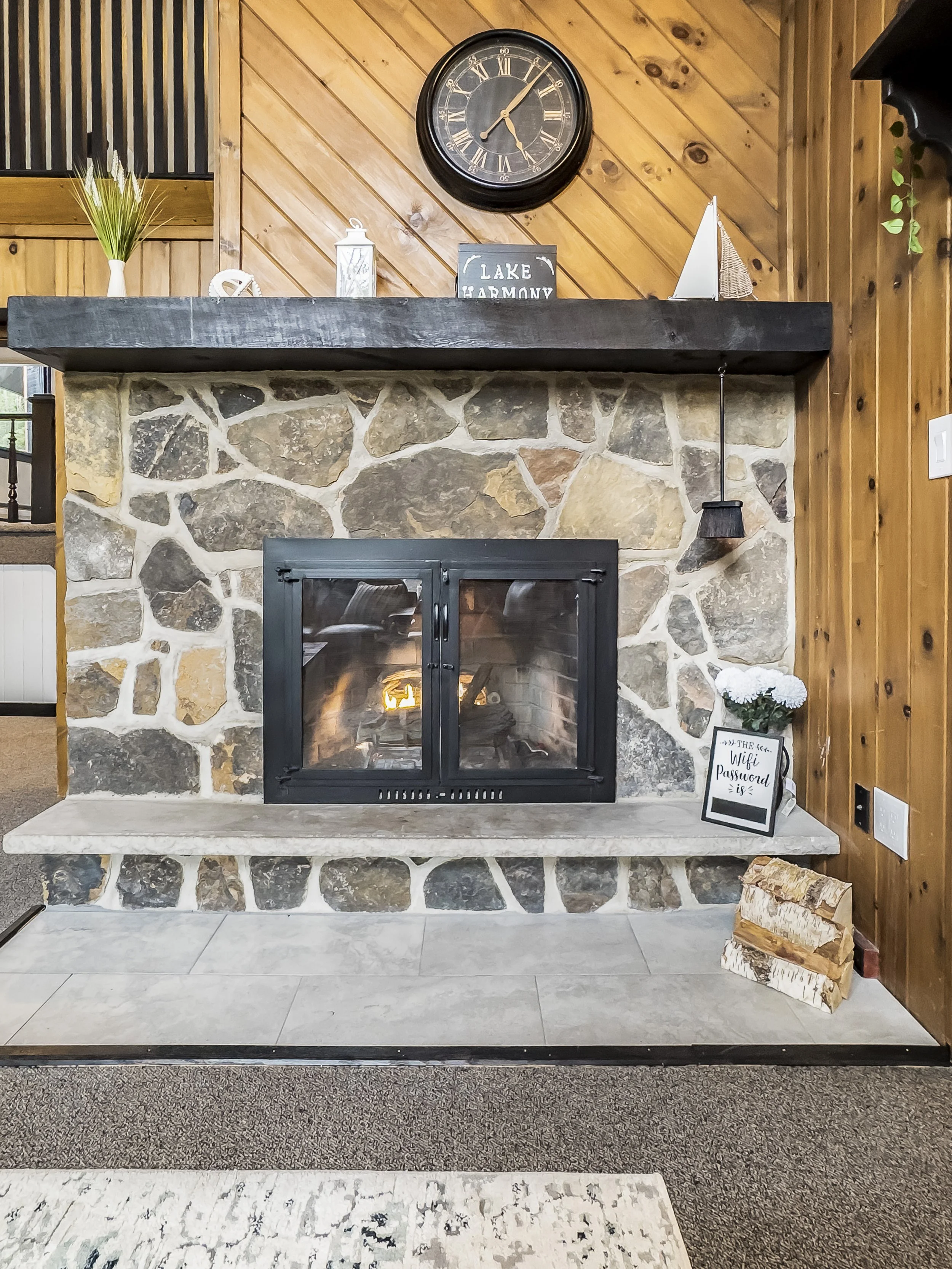 A stone fireplace with a black mantel and a large black clock above it. 