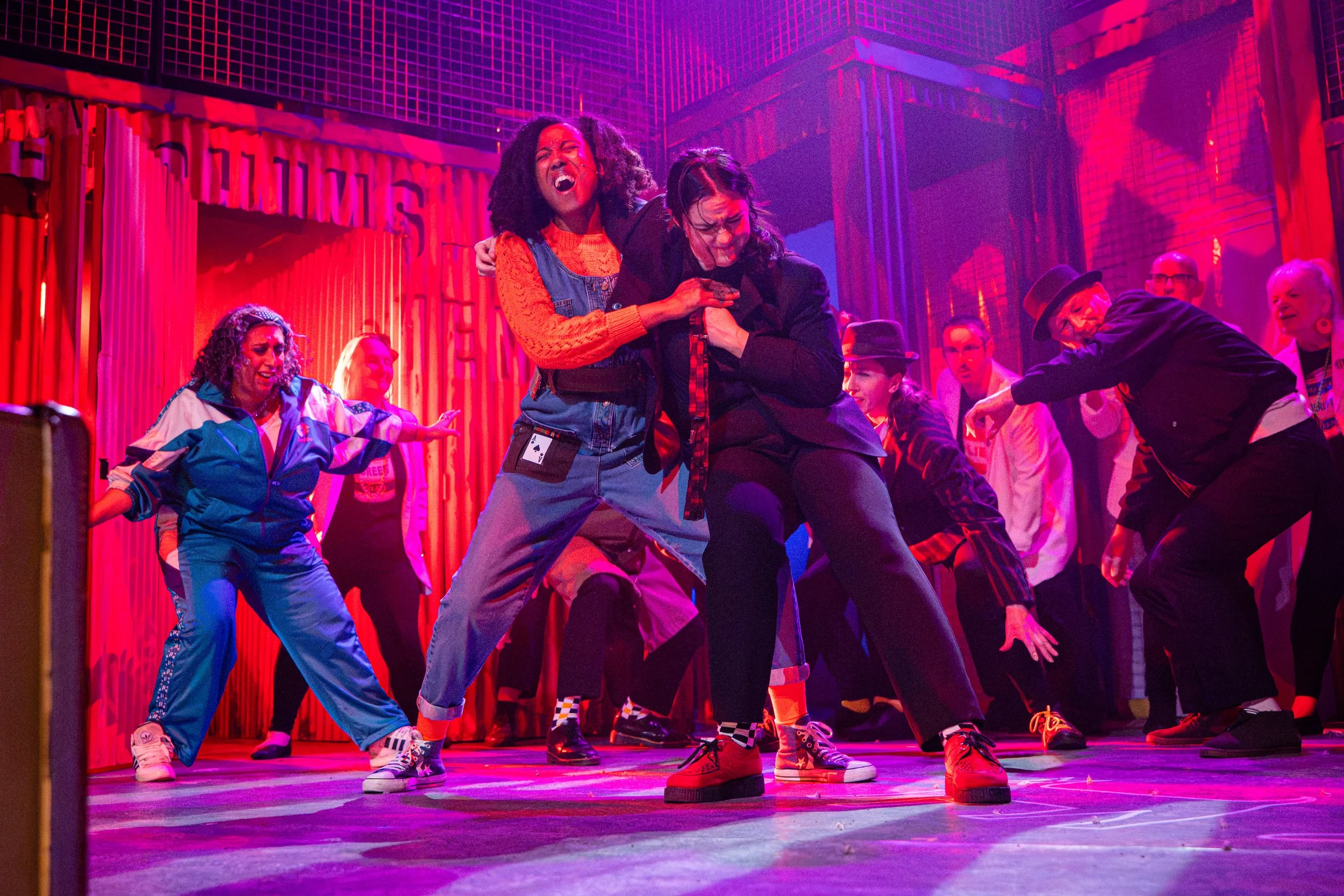 People fighting on stage with red and pink lighting, with shocked and tense expressions.