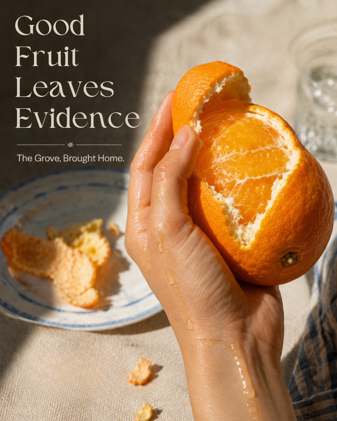 A hand peeling an orange with juice dripping down, with a plate of orange peels and a glass of water in the background.