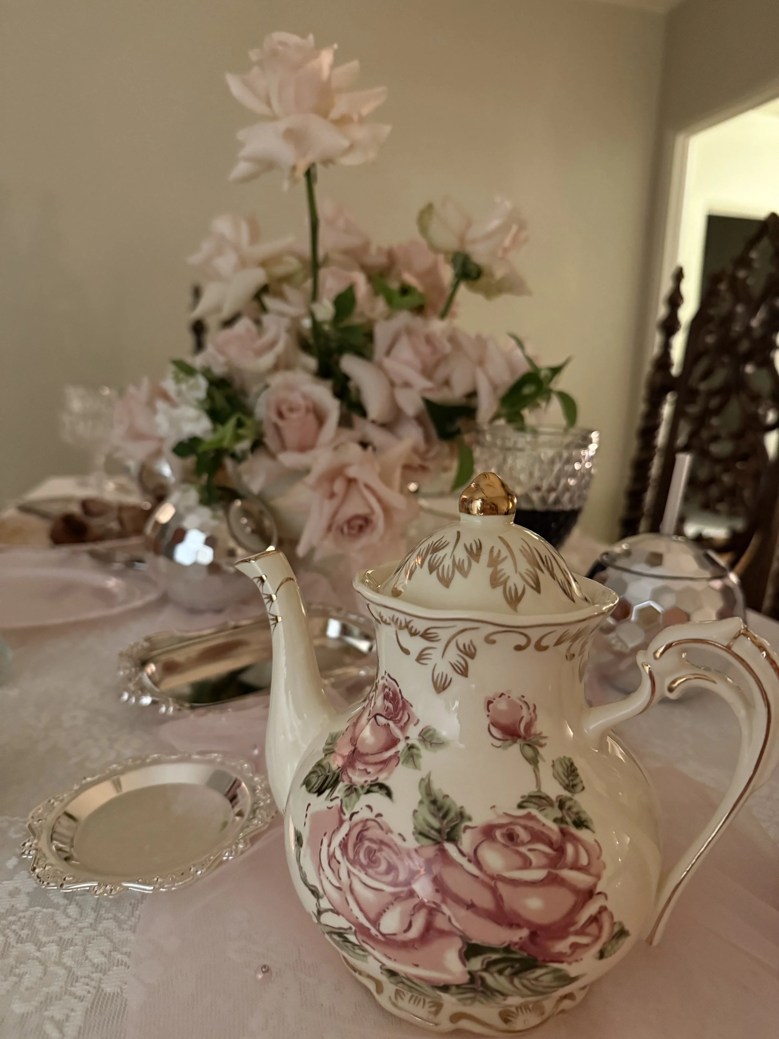 Elegant tea set with floral design, positioned in front of a bouquet of pink and white roses on a dining table.
