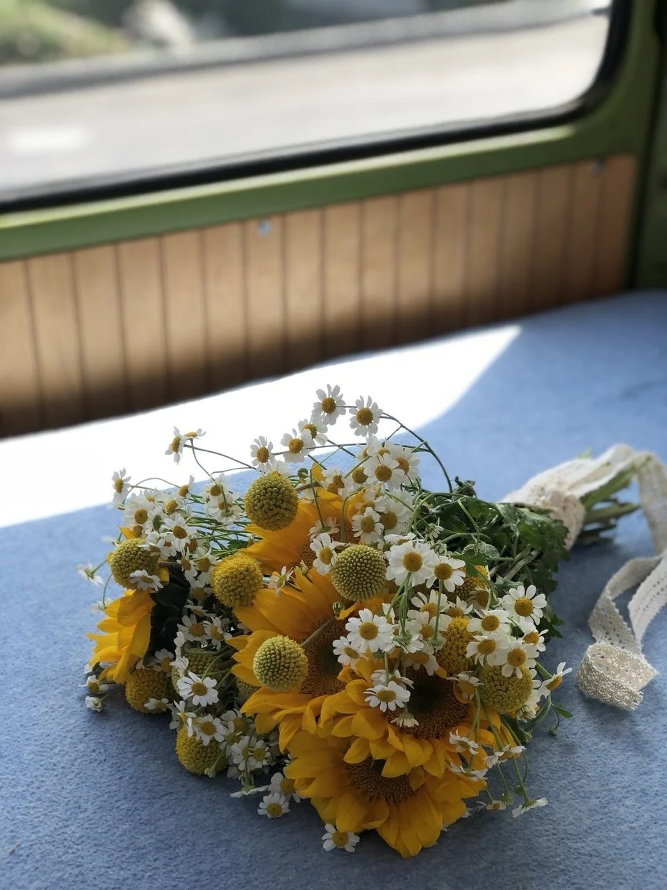 Bouquet of yellow sunflowers and small white daisies with green stems placed on a blue surface near a window