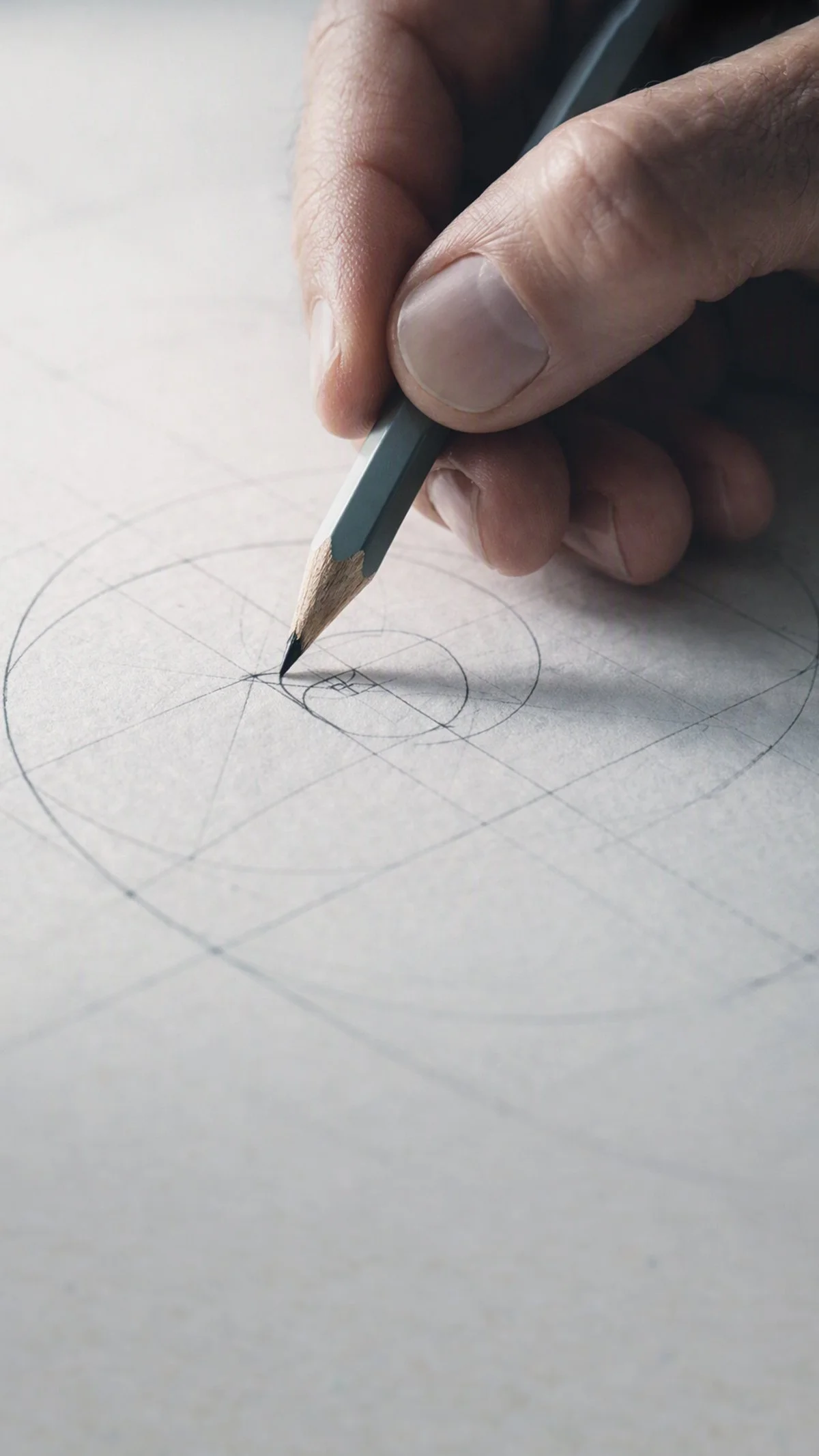 Close-up of a person holding a pencil and drawing geometric circles and lines on white paper.