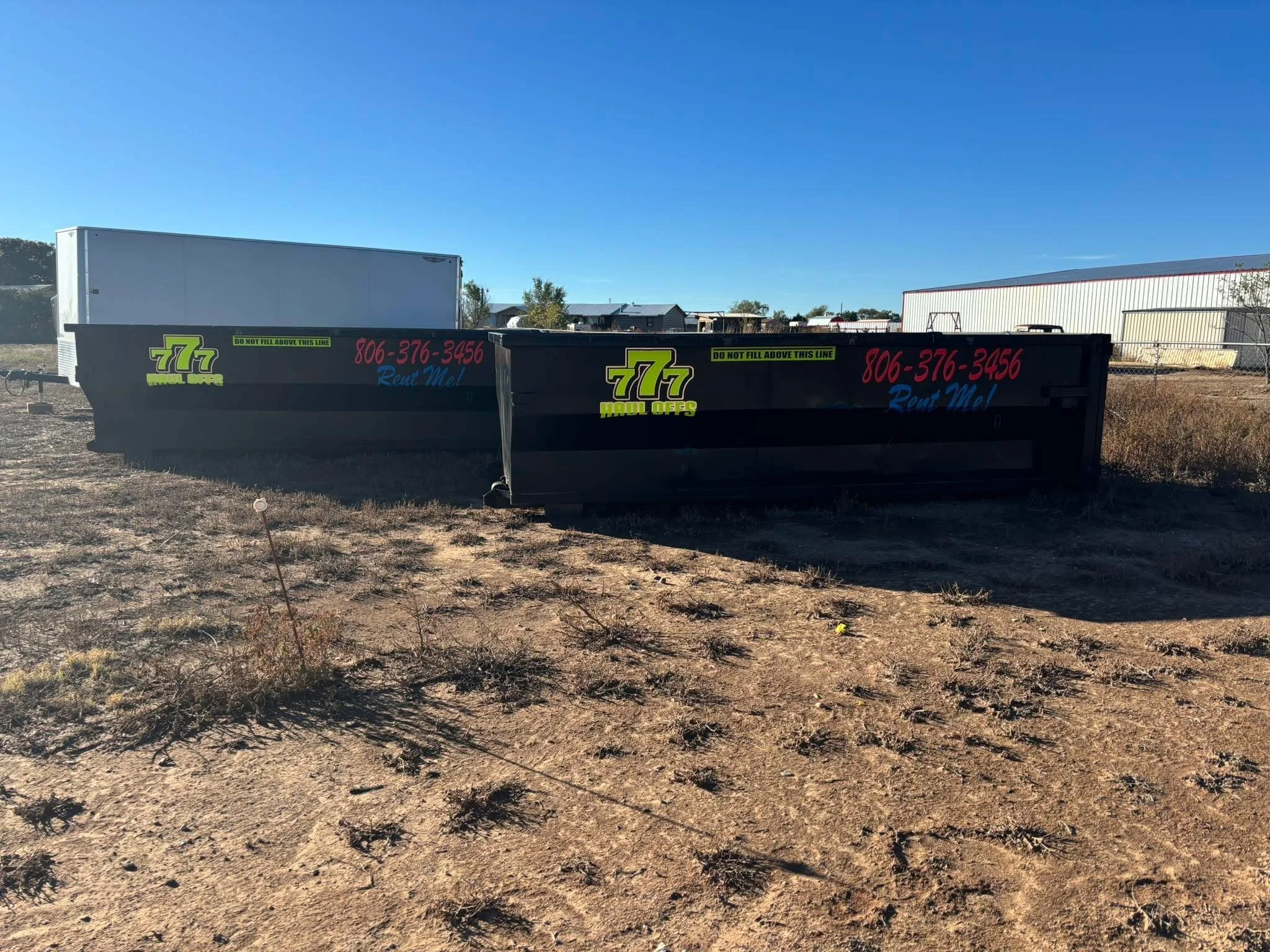 Two black 777 roll-off dumpsters staged side by side on a Texas Panhandle job site
