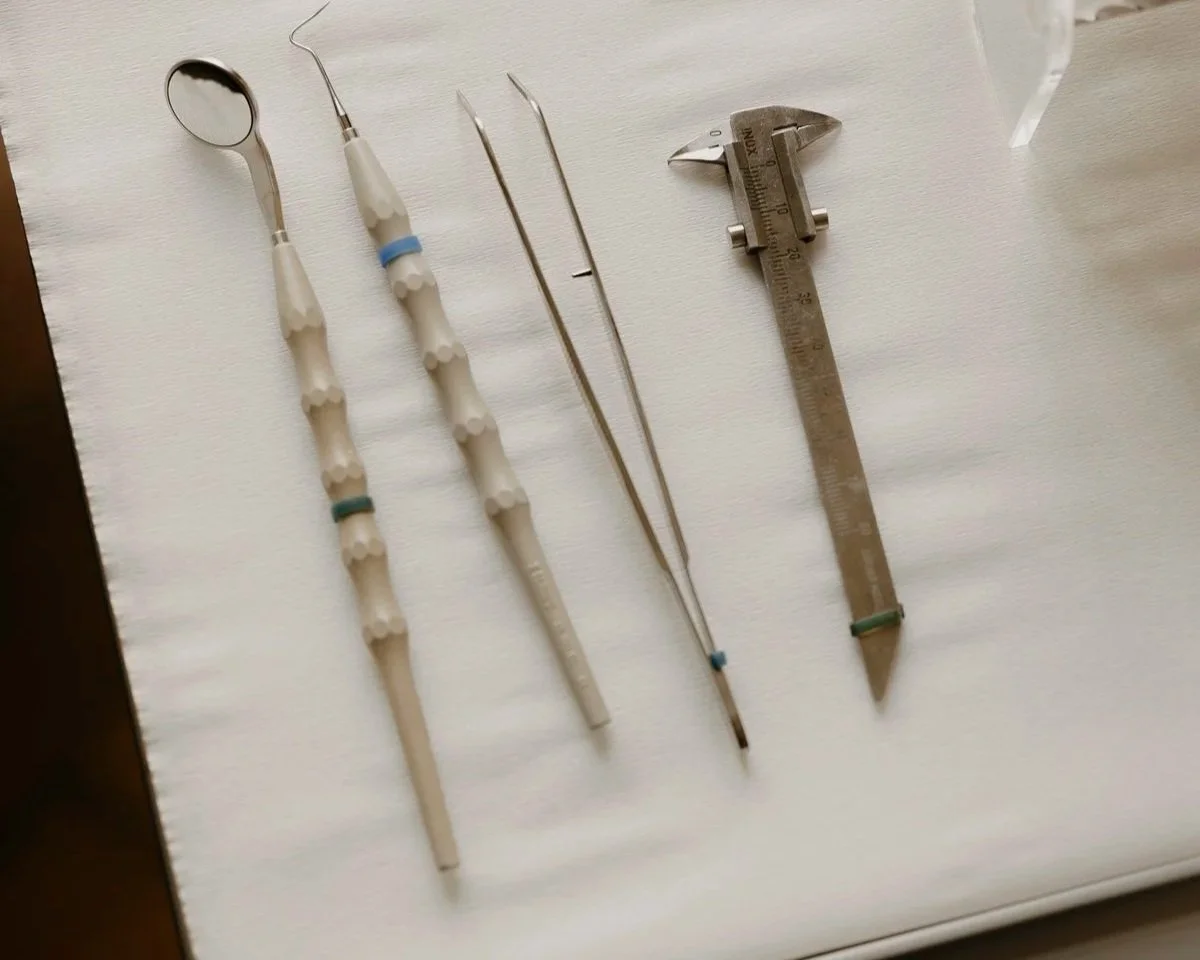 Medizinisches Instrumenten-Set, including Spiegel, Zange, Pinzette, und Messgerät auf weißem Tuch.