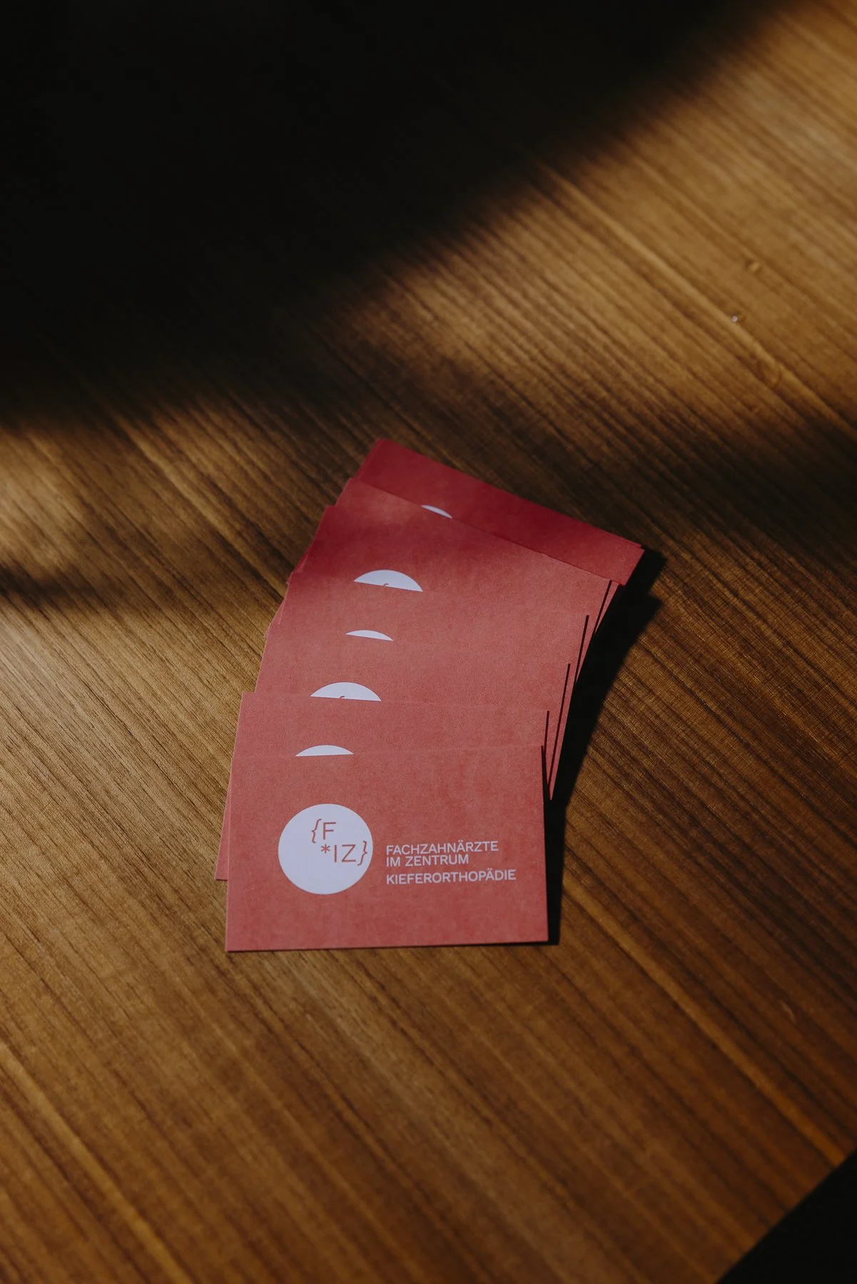 Mehrere rote Visitenkarten mit weißem Logo und Text auf einem Holztisch liegen.