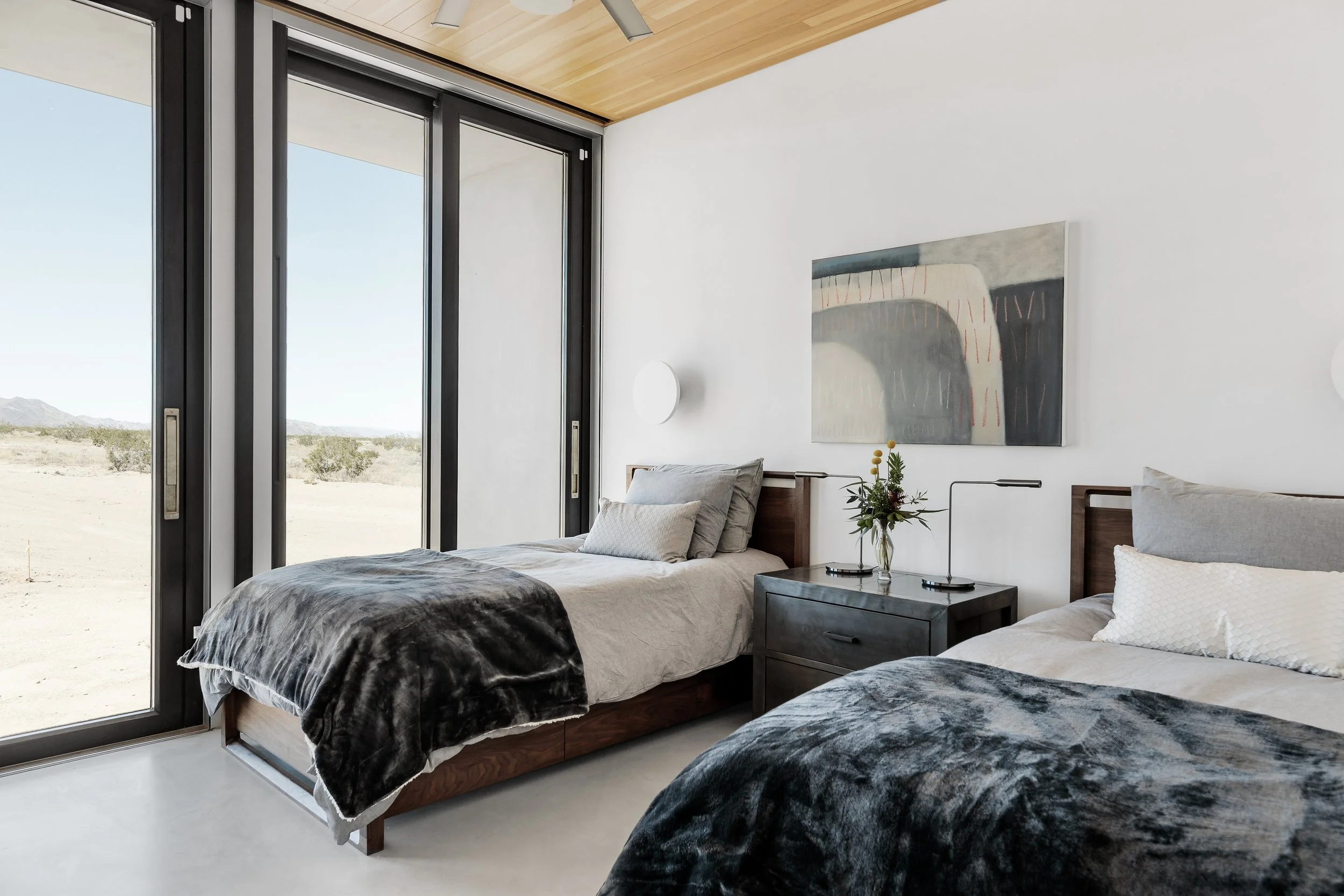 Modern bedroom with two beds, large sliding glass doors, and desert landscape view.