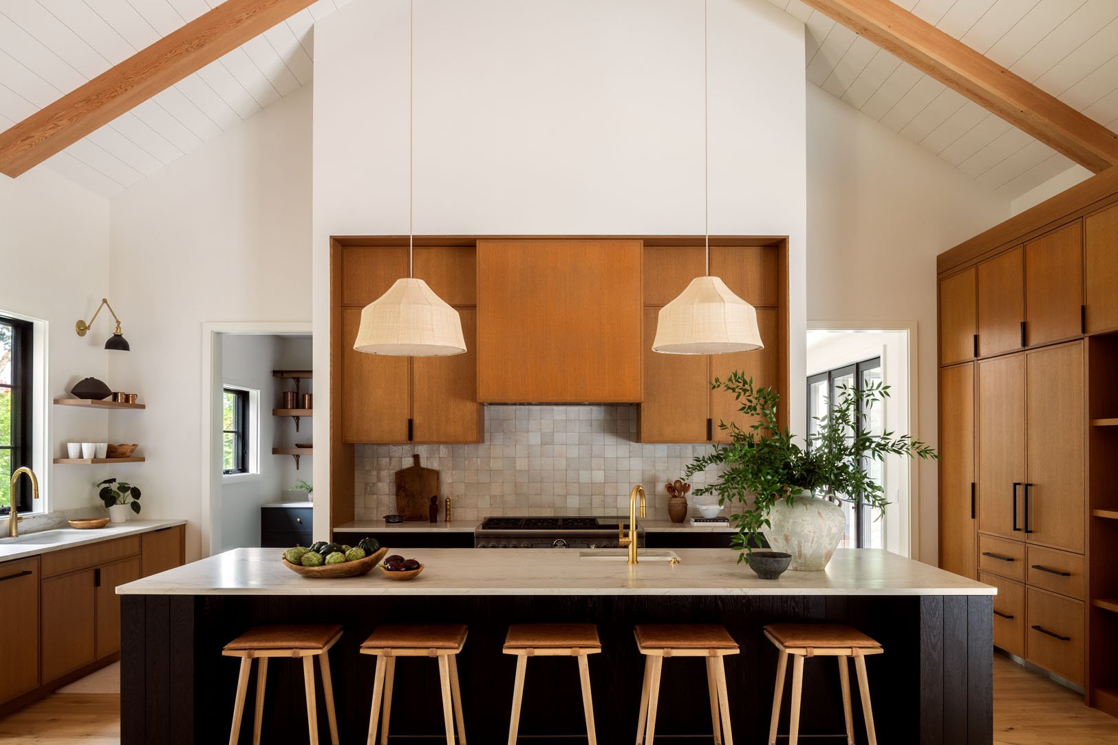 Modern kitchen with wooden cabinets, a large island with a white countertop, pendant lights, and natural light from windows.