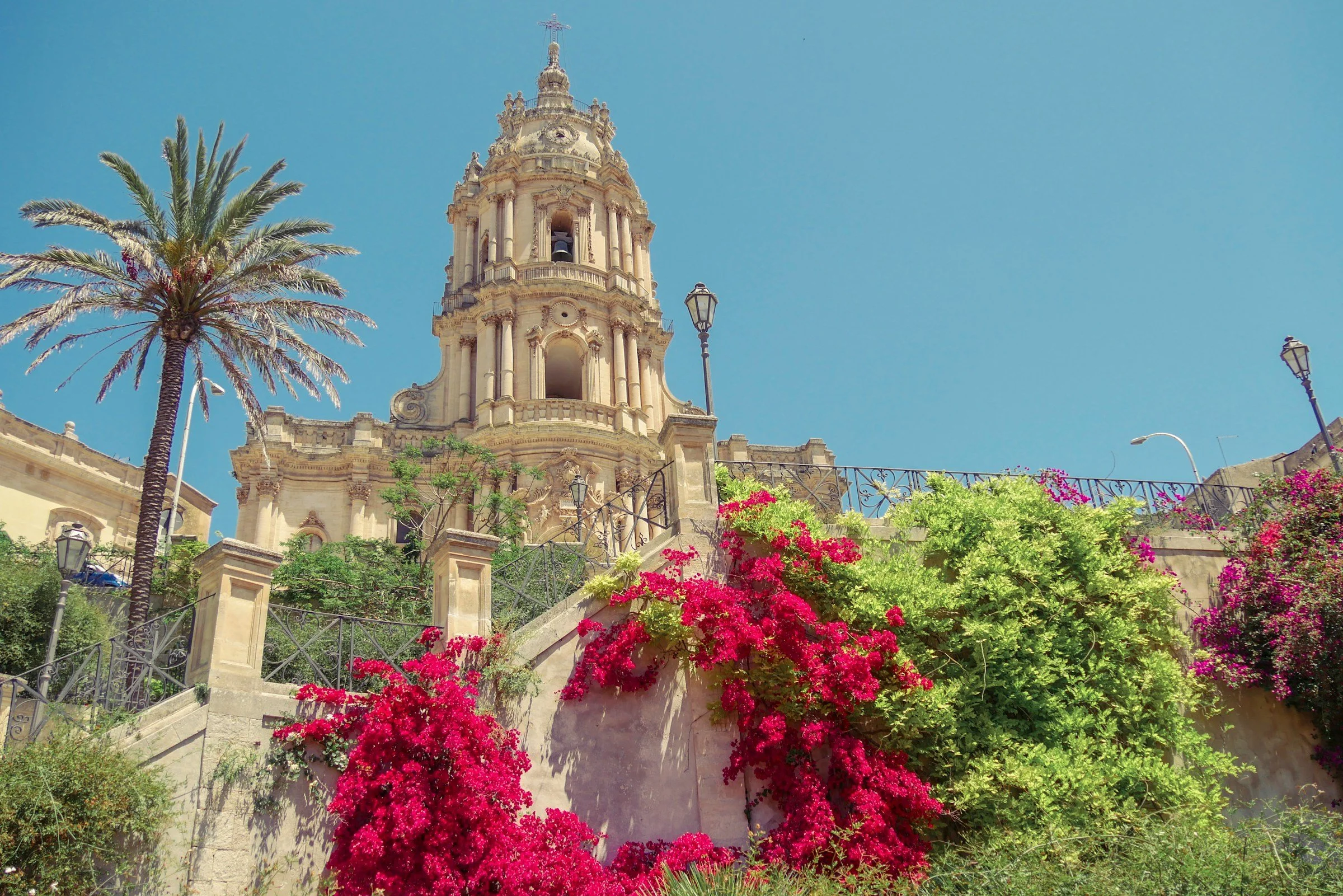 Historic Sicilian architecture framed by palm trees and flowering bougainvillea, reflecting the island’s cultural heritage and landscape